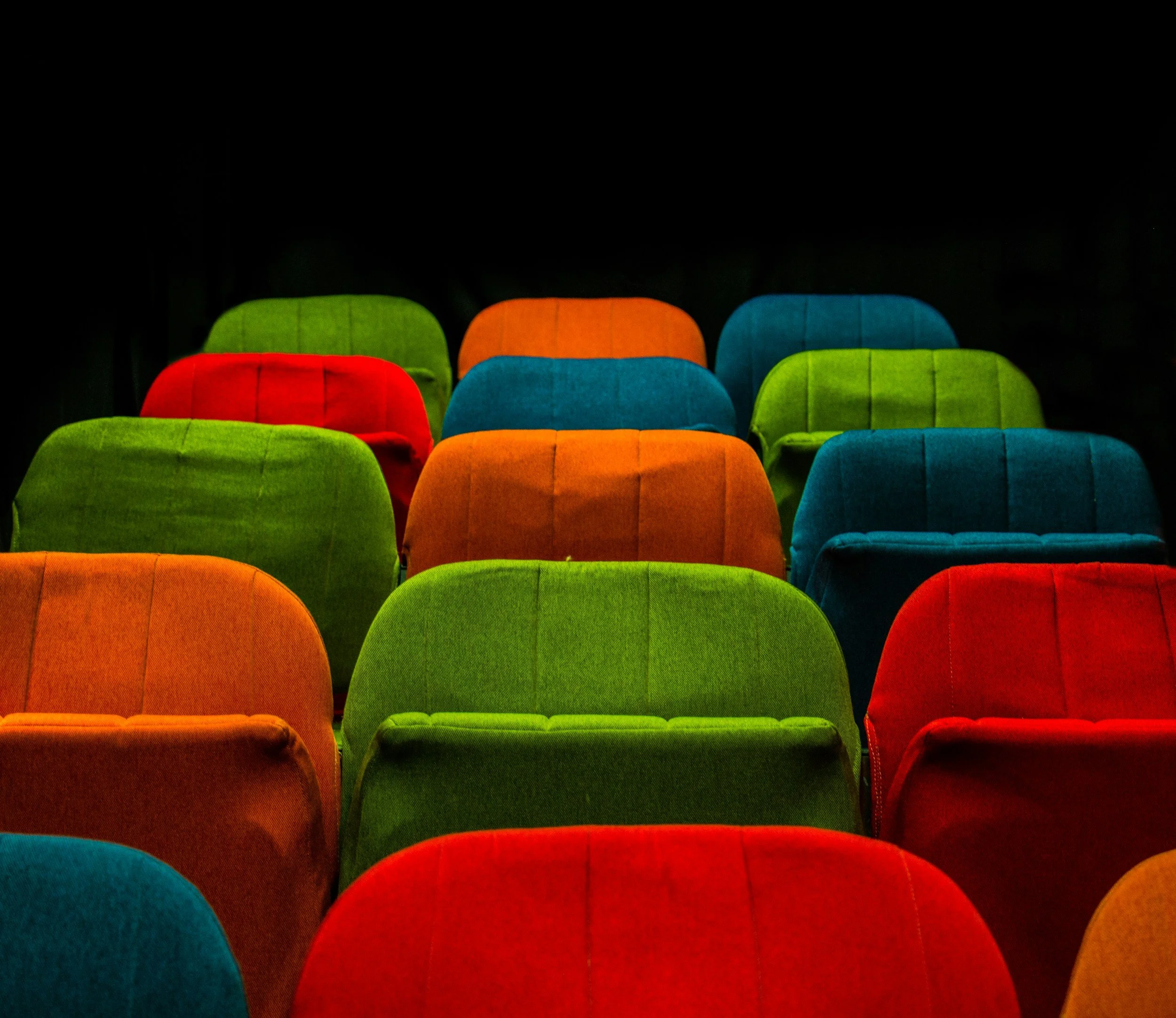 Multiple colorful chairs arranged in rows on a black background.