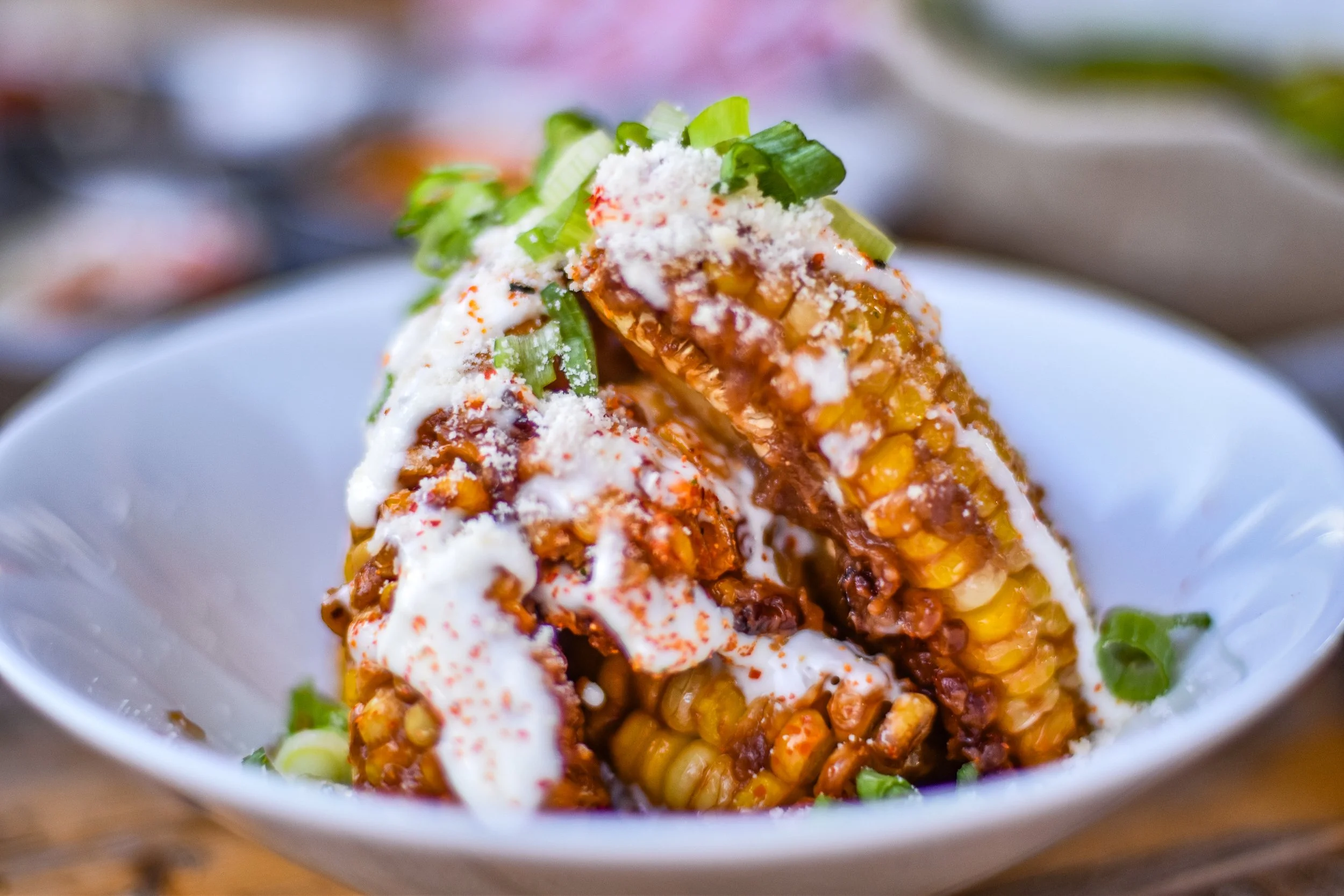 Close-up of Mexican street corn (elote) in a white bowl, topped with mayonnaise, cheese, chili powder, and chopped green onions.