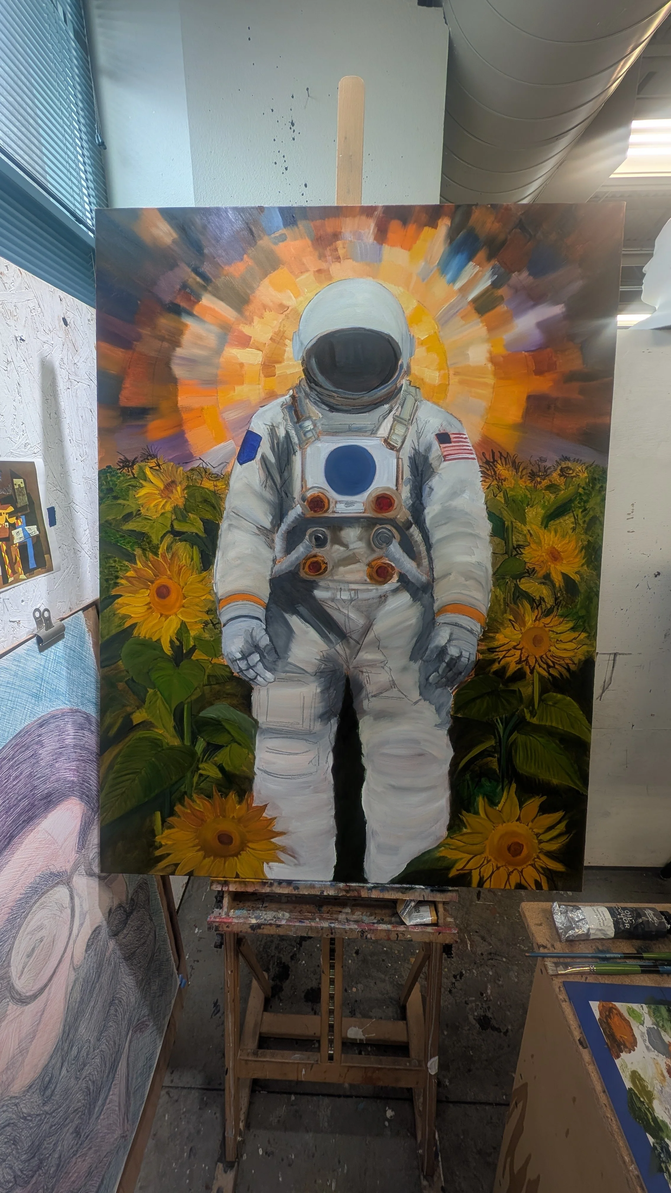 Painting of an astronaut standing among sunflowers with a colorful abstract background, displayed on an easel in an art studio.