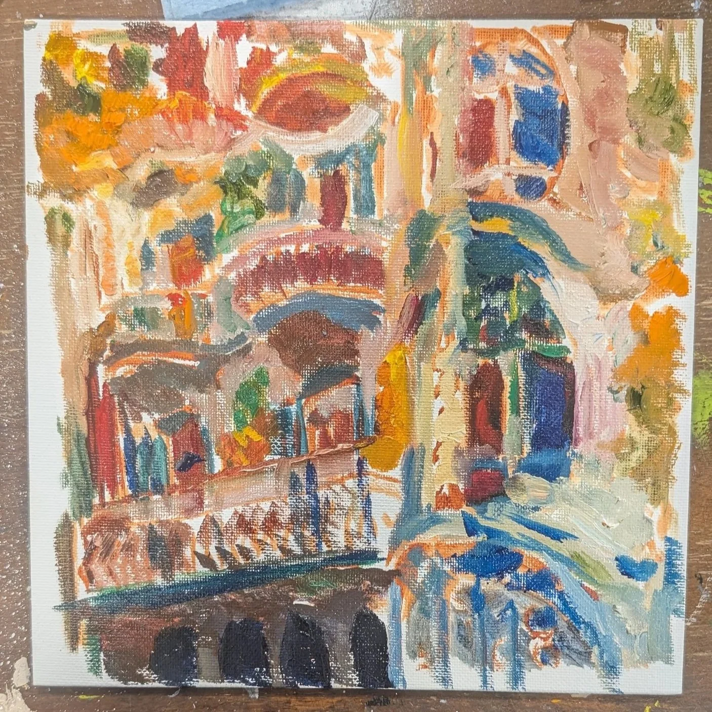 An abstract impressionist painting of a city scene featuring a bridge over a canal, with buildings and trees in warm colors like orange, red, yellow, and green, and a blue sky in the background.