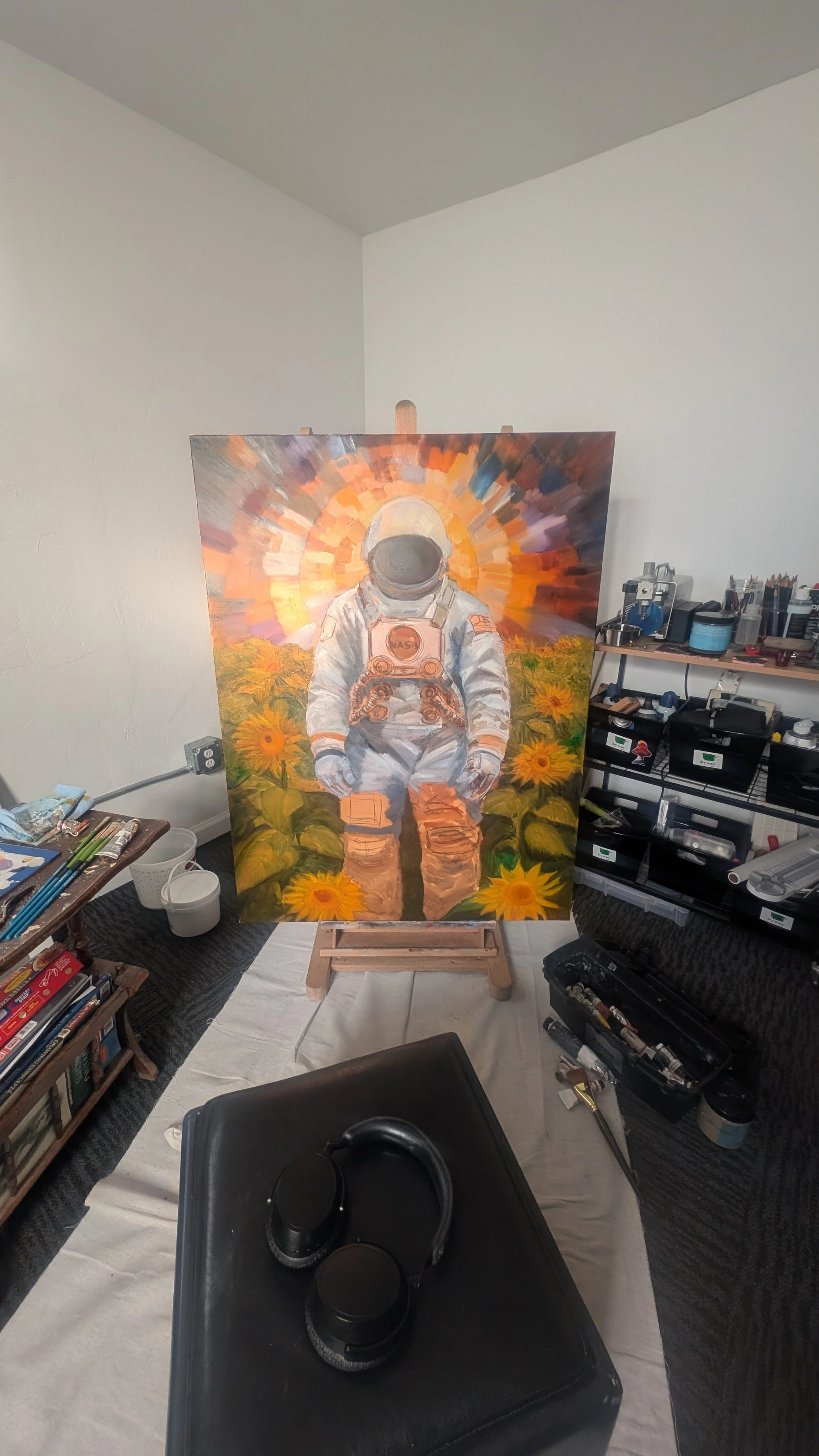 An unfinished painting of an astronaut standing in a sunflower field with a colorful, radiant background on an easel in an art studio.
