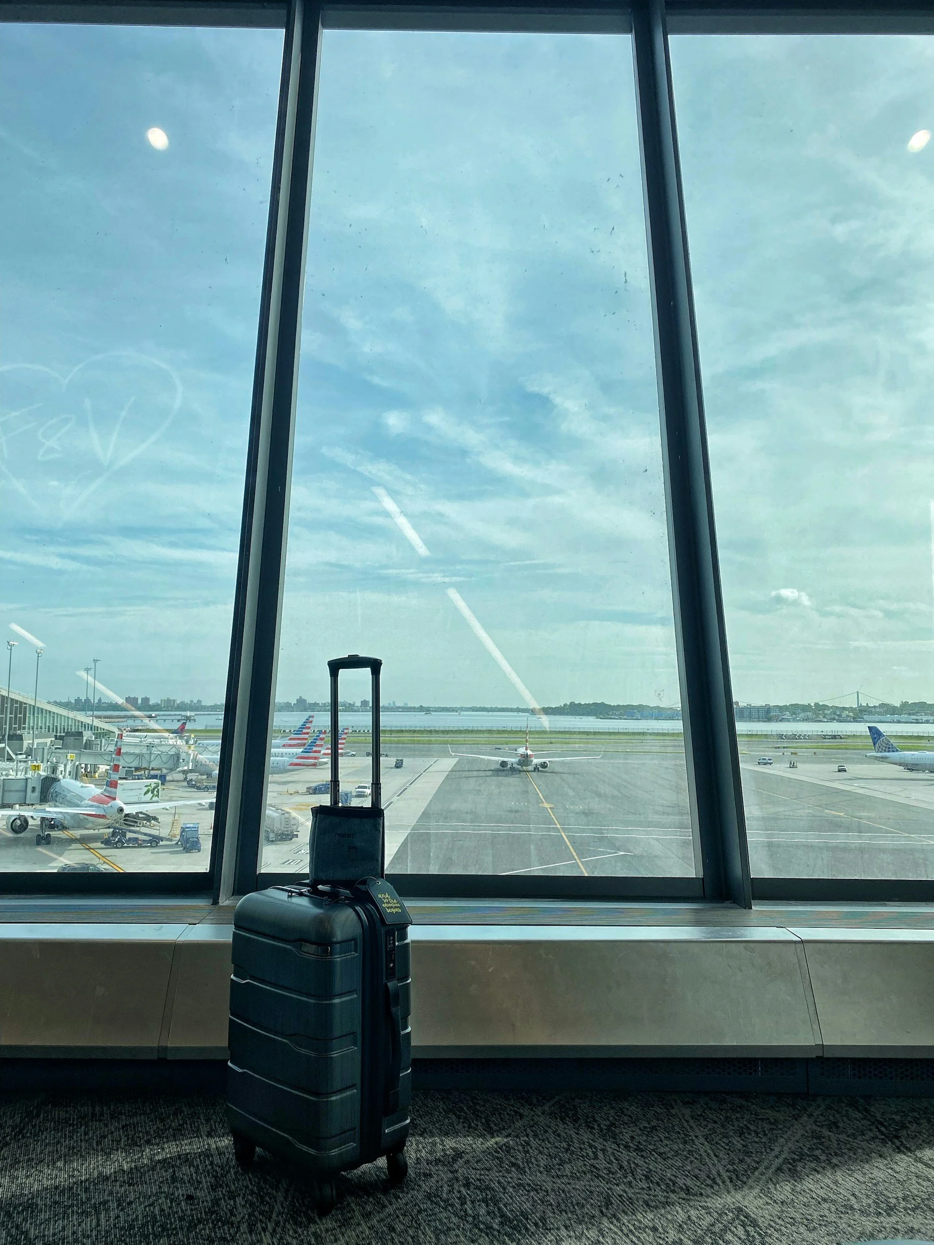 View from airport terminal window showing taxiing airplanes, parked planes, and a blue sky with few clouds.