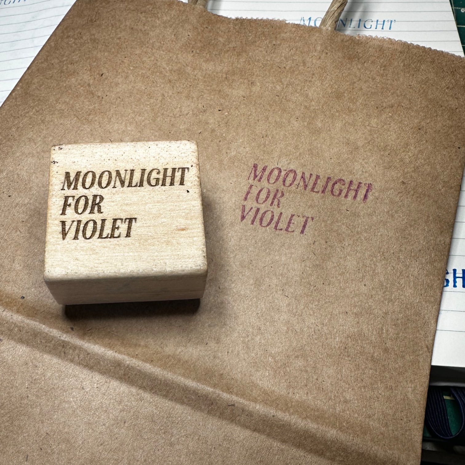 A rubber stamp with the words 'MOONLIGHT FOR VIOLET' is stamped on a brown paper surface, with an identical stamped impression to its right.