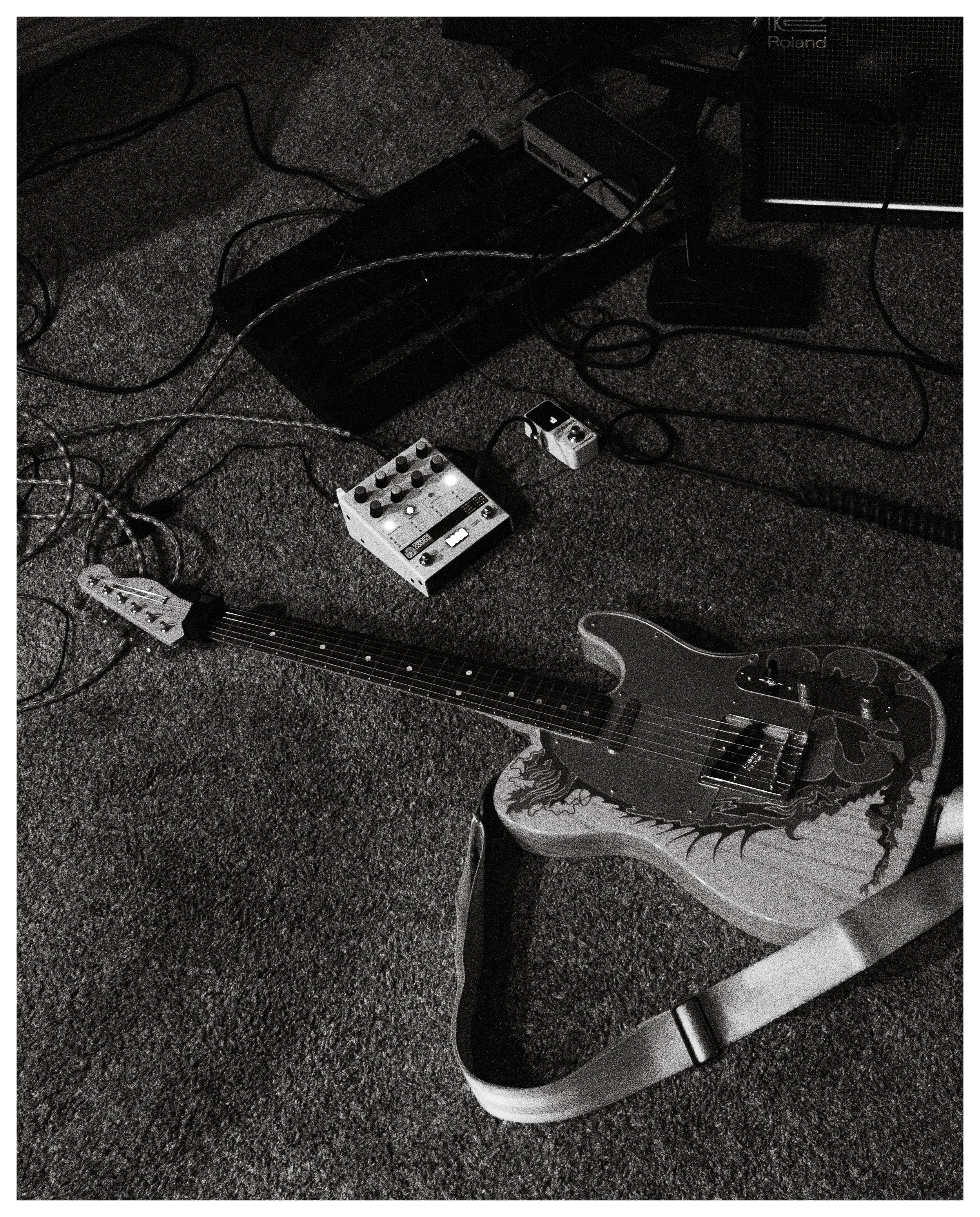 An electric guitar with a dragon design on the body, connected to guitar pedals and an amplifier in a music setup.