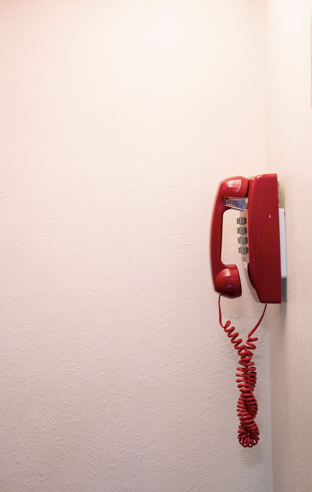 Red rotary telephone mounted on a light pink wall.