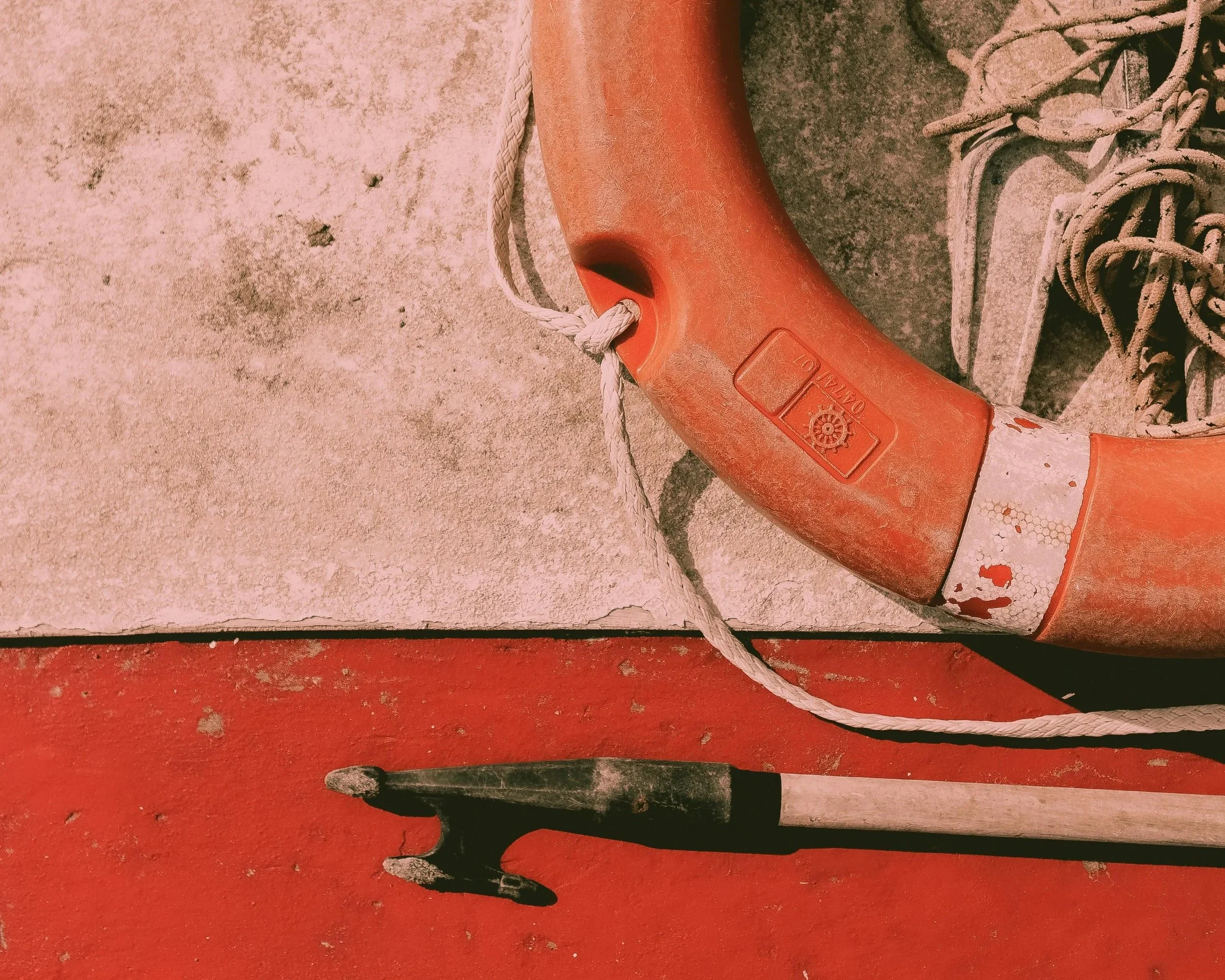 A life preserver ring with rope attached and a hammer lying nearby on a red surface, with gray tiled flooring in the background.