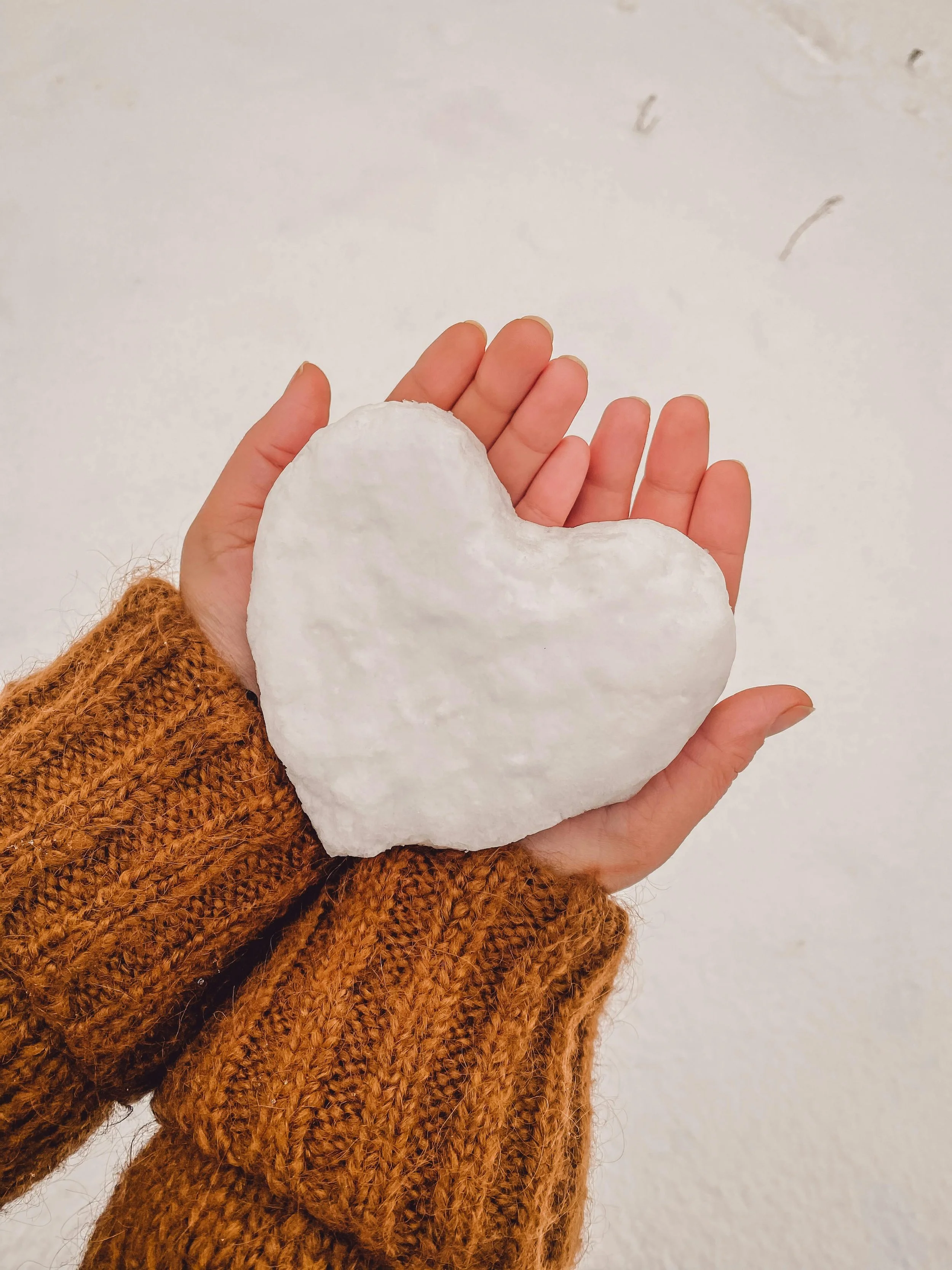 Person holding a large, white heart-shaped object in one hand, wearing a brown knitted sweater.