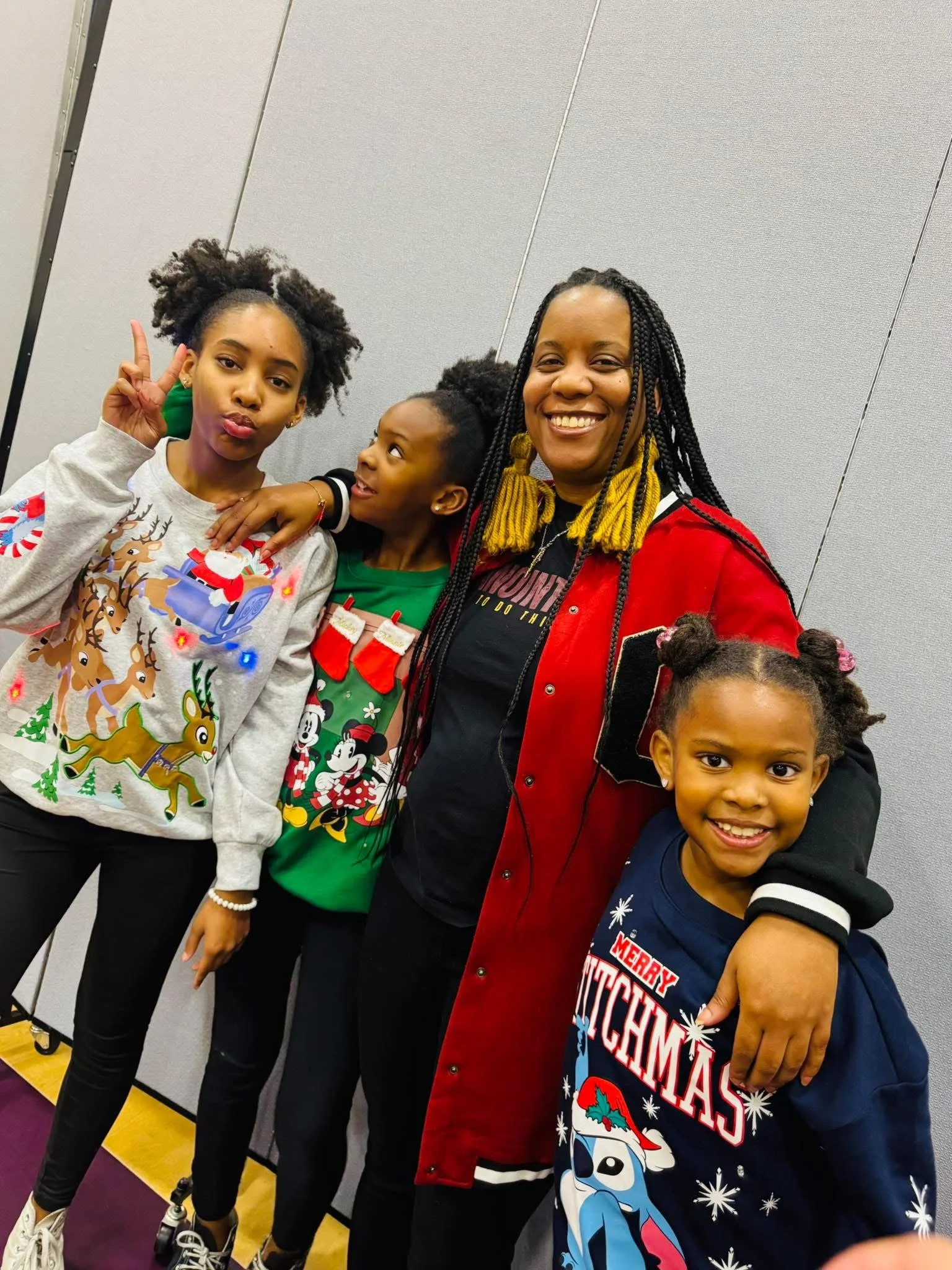 A woman and three children posing together at a festive event, wearing Christmas-themed clothing and smiling.