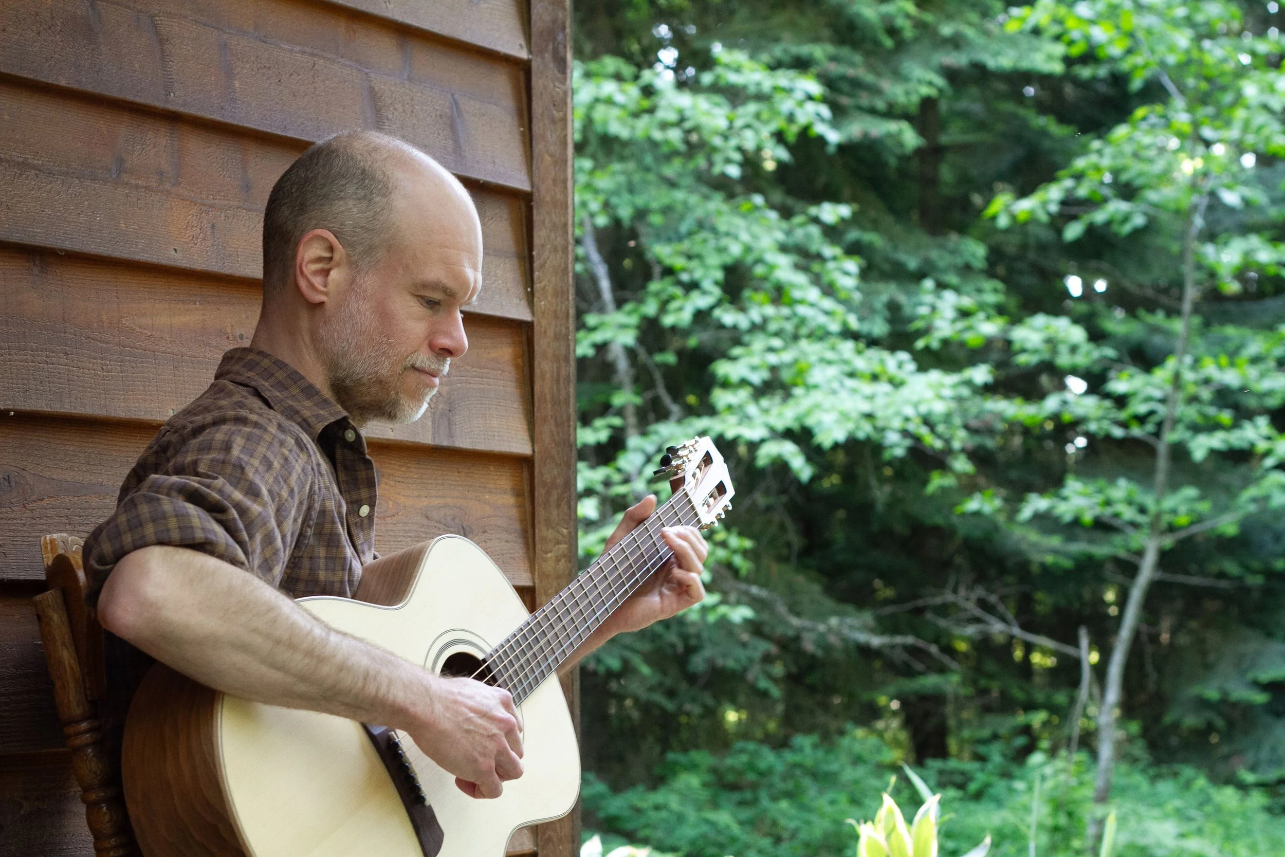 A man plays guitar with trees in the background