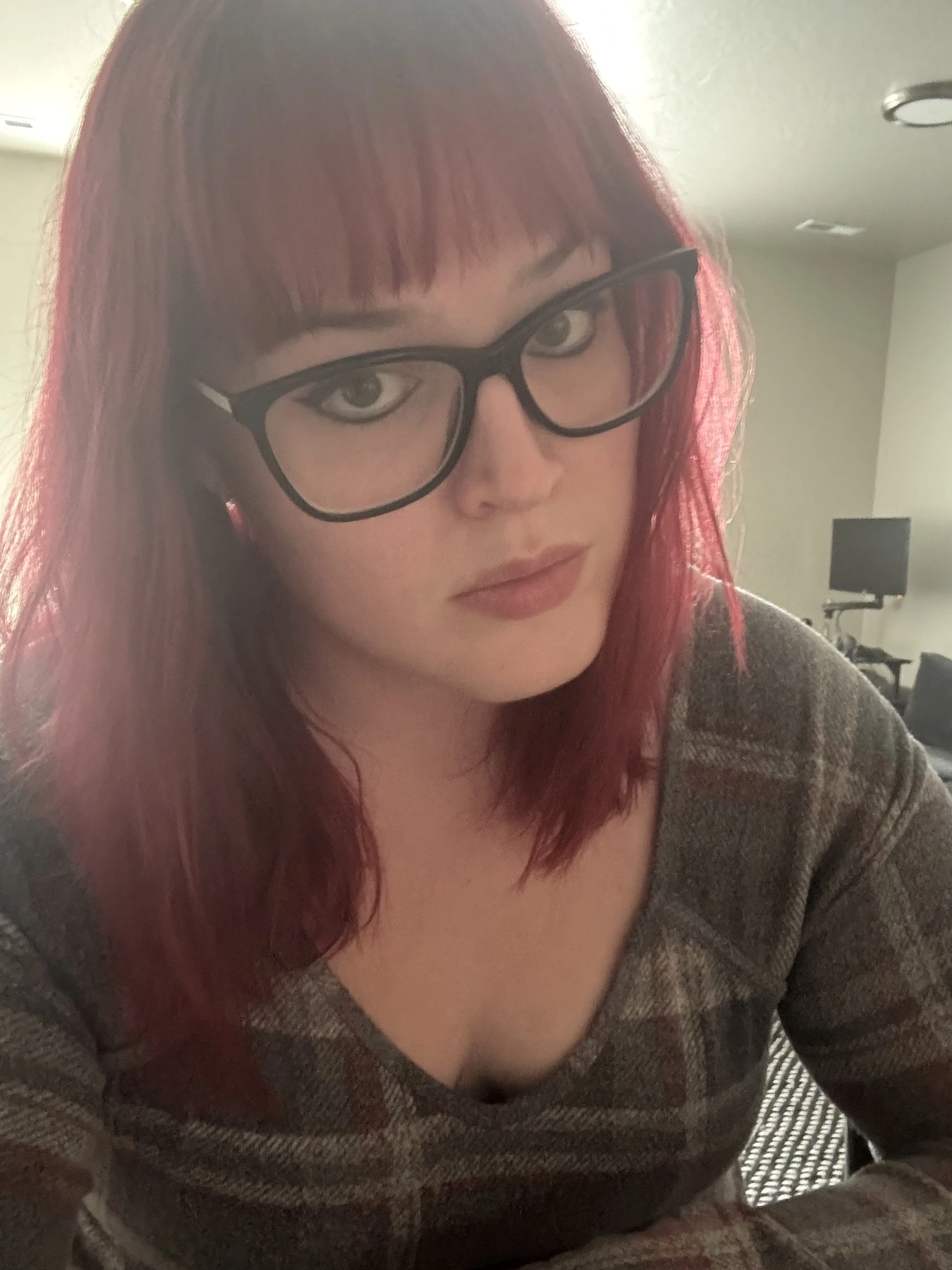A person with glasses and dark pink hair looks at the camera