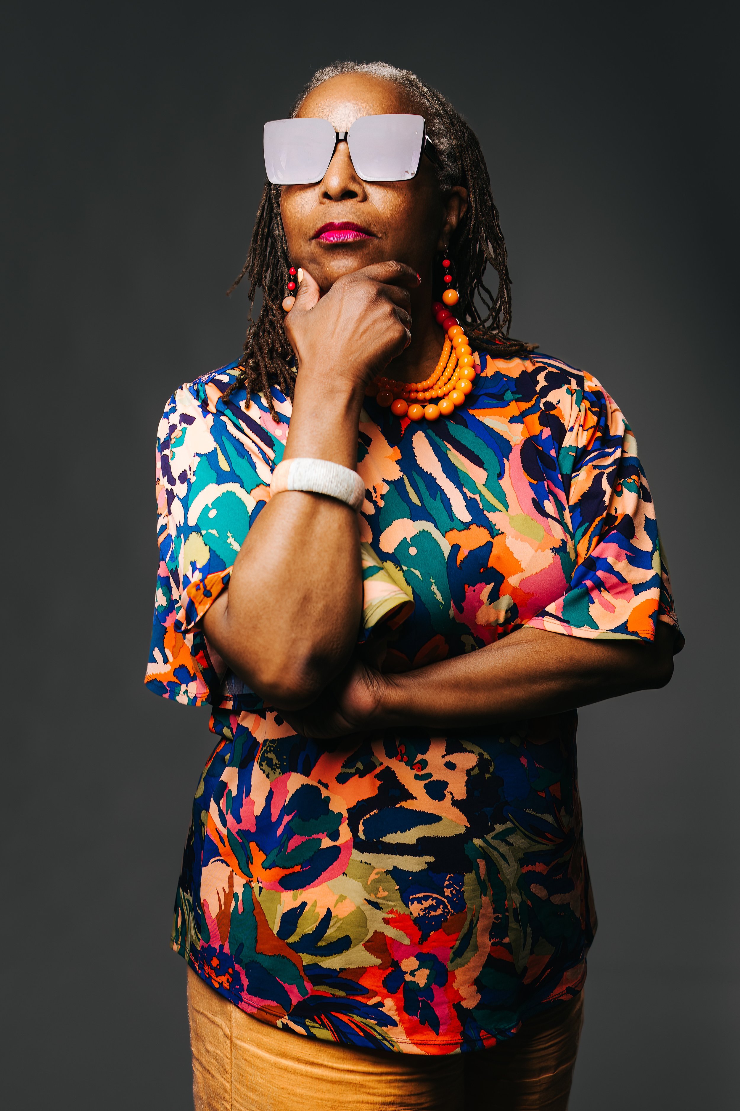 A black woman with wicked rad shades and a bright shirt looks badass