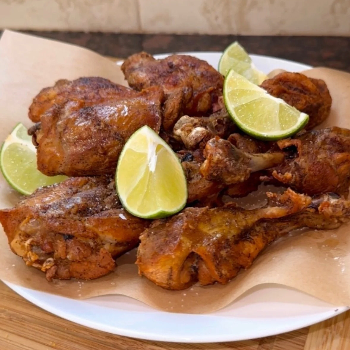 Plate of seasoned, fried chicken pieces garnished with lime wedges.