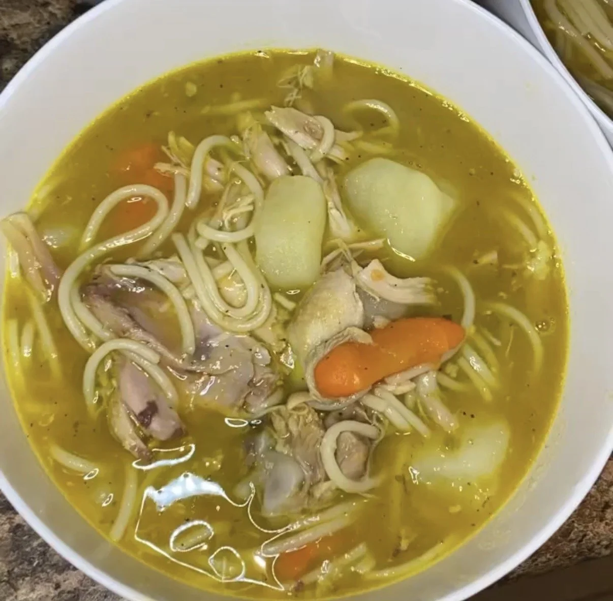 A bowl of chicken noodle soup with carrots, potatoes, and shredded chicken in a broth.