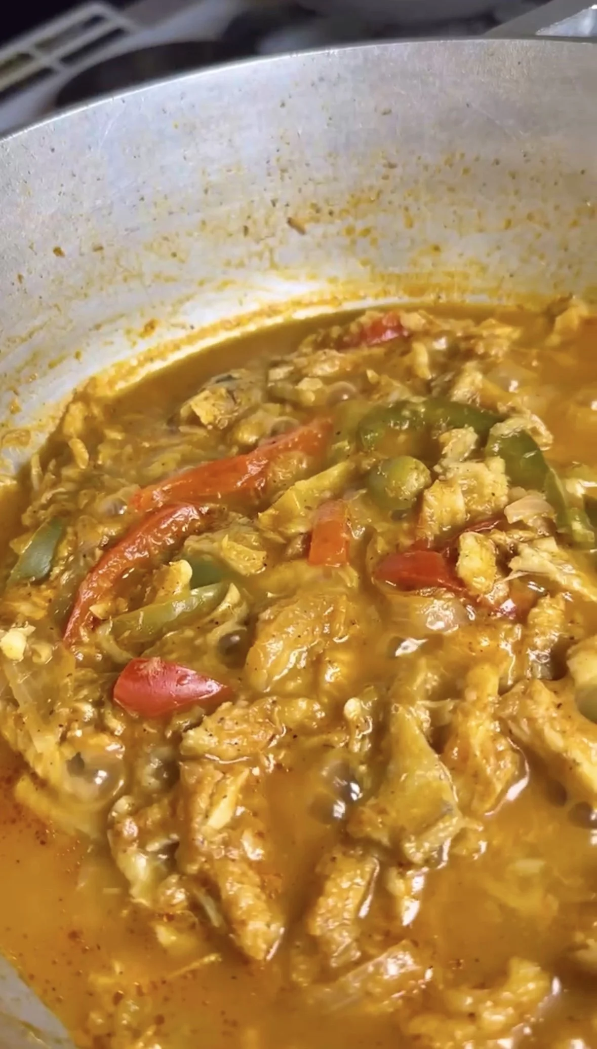 A pot of cod stew with vegetables, including red and green bell peppers, and cod pieces in a thick, savory sauce.