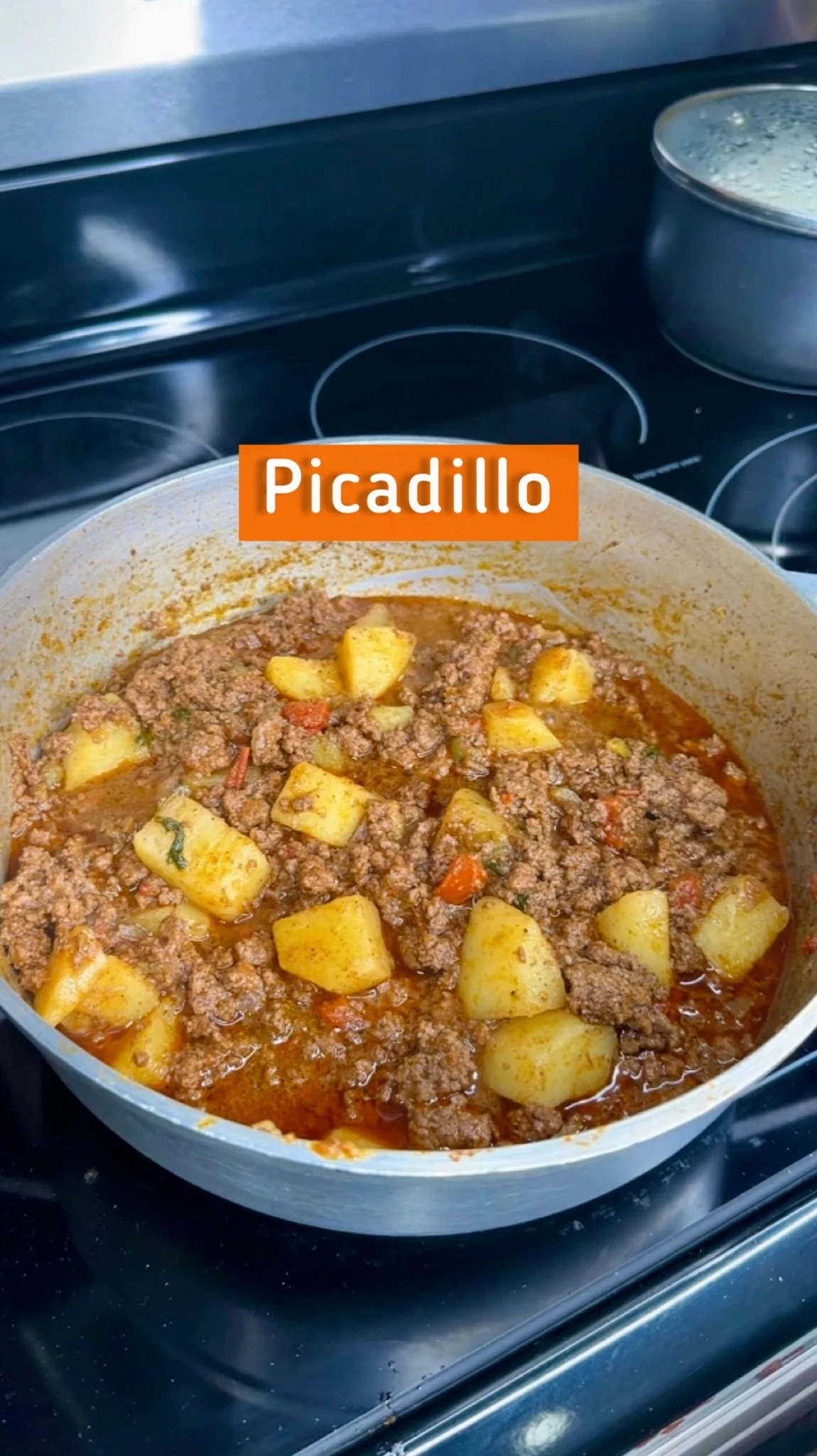 Pot of ground beef and potato stew on a stove with a label 'Picadillo'.