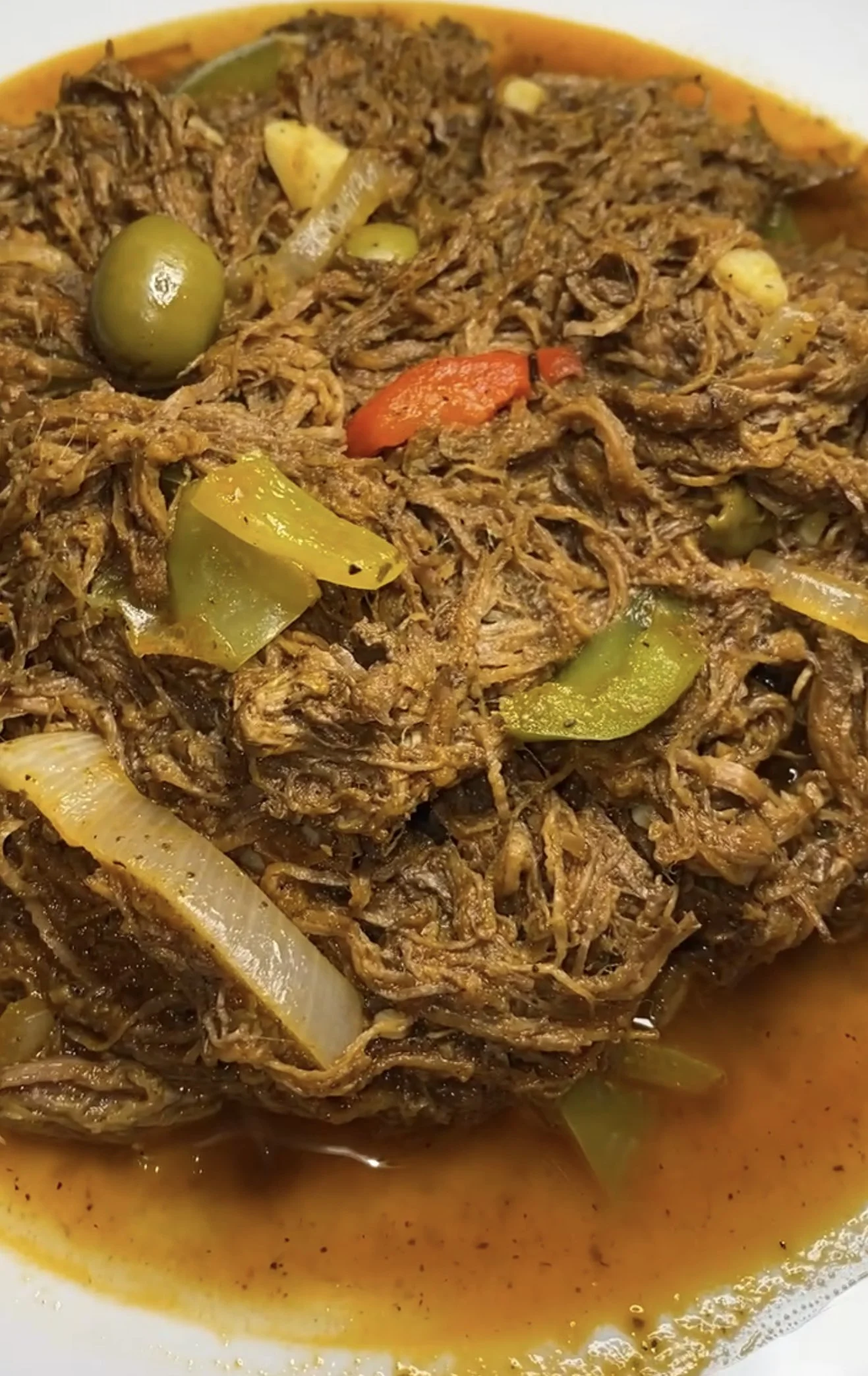 A plate of shredded ropa vieja with green bell peppers, onions, and gravy.