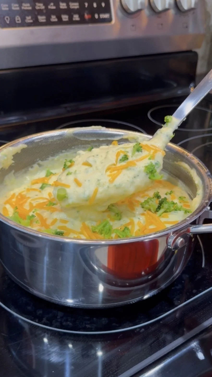 A stainless steel pot of homemade cheesy potato soup with green onions on top on an electric stove.