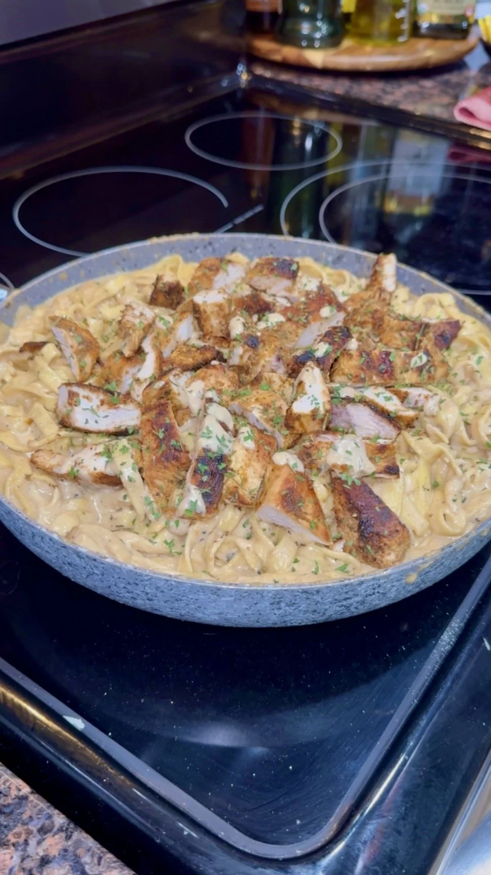 Creamy chicken and pasta dish topped with grilled chicken pieces, garnished with chopped herbs, on a stovetop.