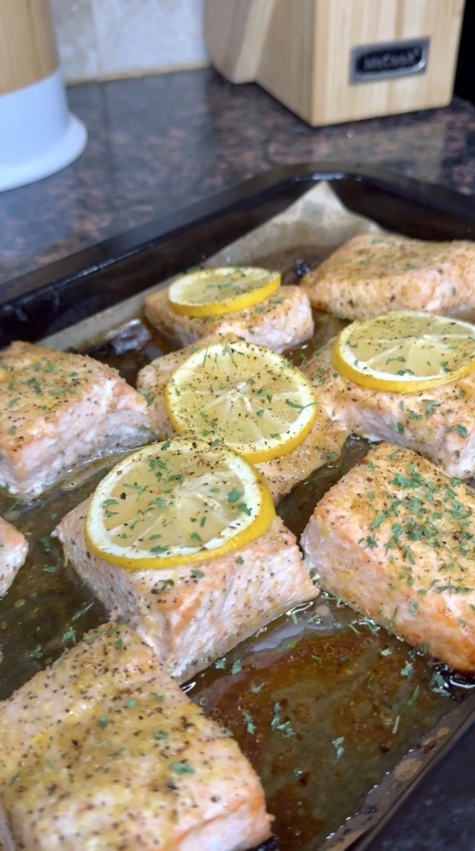 Baked salmon fillets topped with lemon slices and herbs on a baking sheet.
