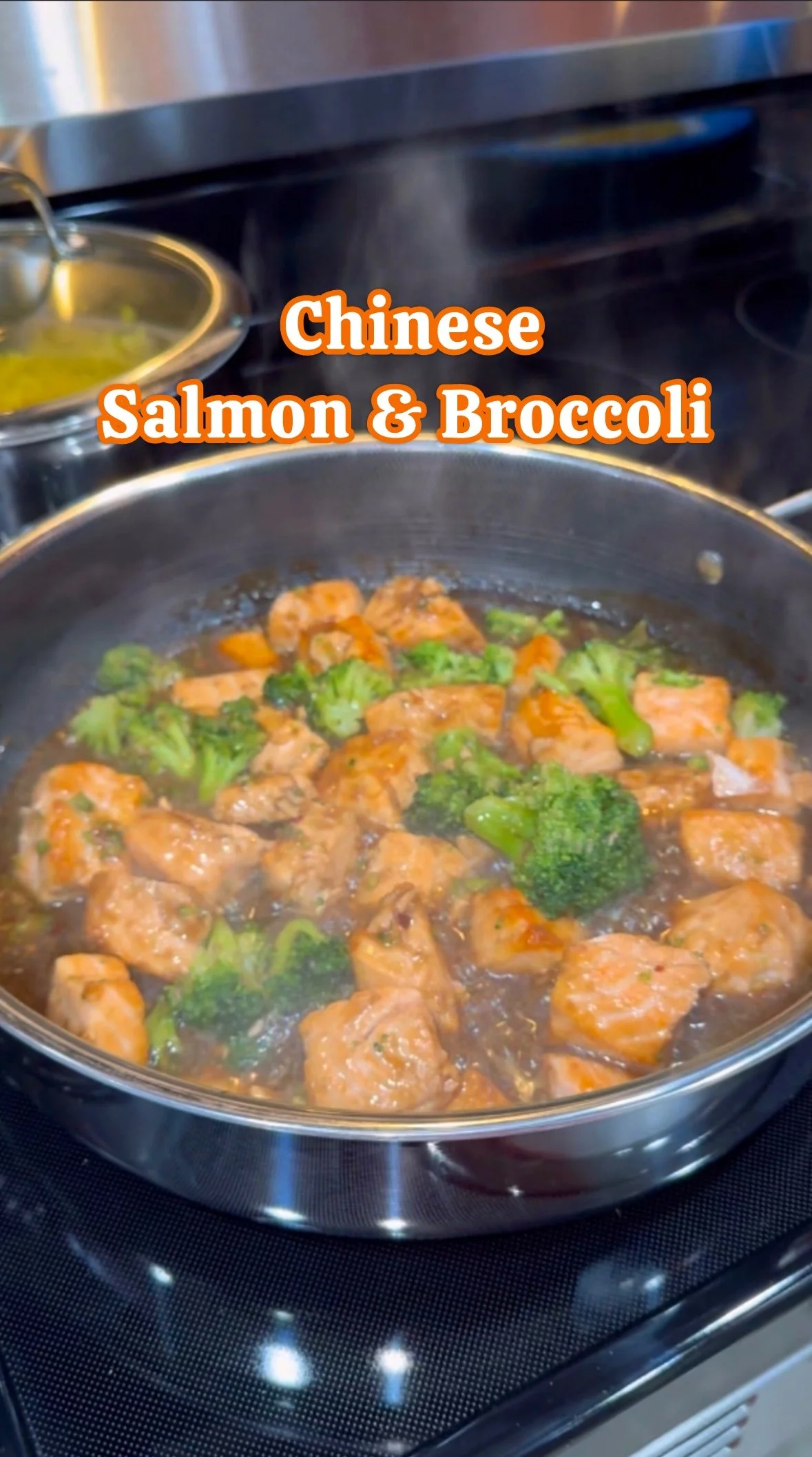 A skillet on a stovetop with pieces of salmon, broccoli, and sauce cooking inside. Text overlay says 'Chinese Salmon & Broccoli'.