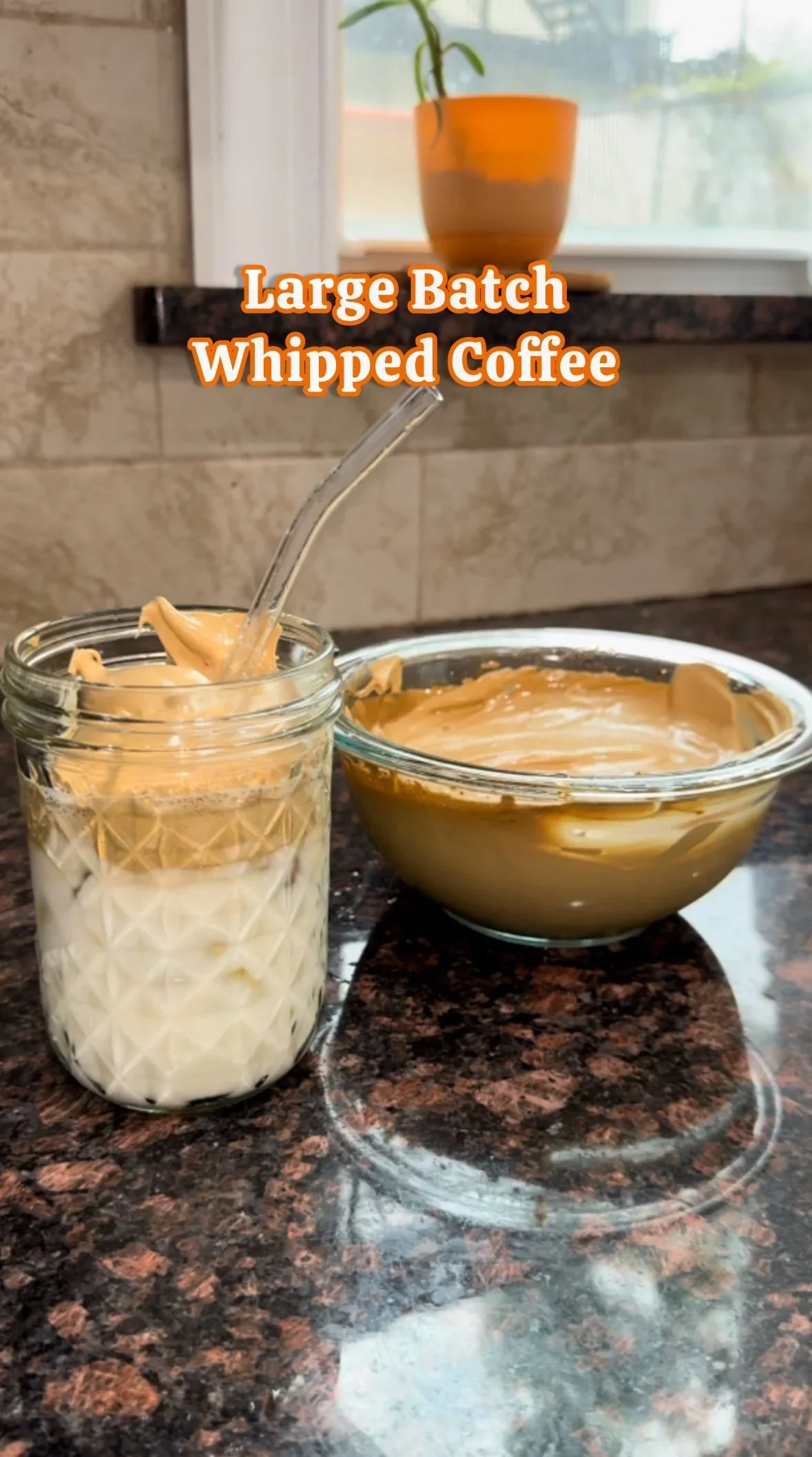 A jar off frozen whipped coffee with a spoon, a bowl of whipped coffee, and a potted plant on a window ledge in the background.