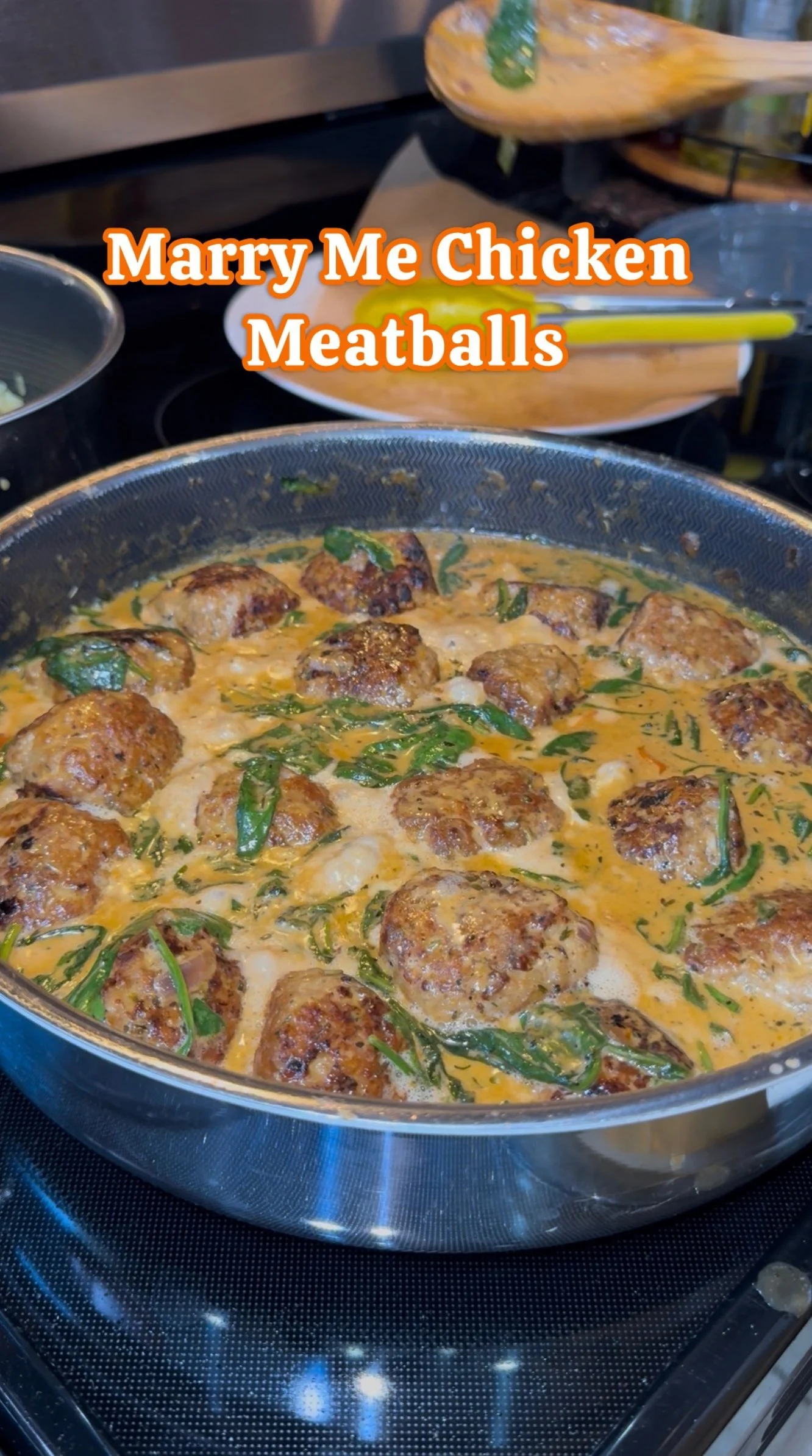 A skillet filled with cooked chicken meatballs in a creamy sauce, garnished with green herbs in a kitchen.