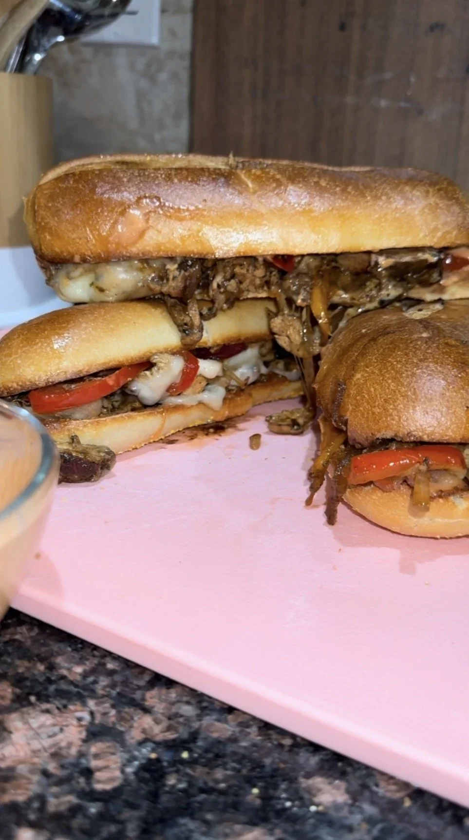 Two subs on a pink cutting board, filled with grilled chicken, cheese, peppers, and onions.