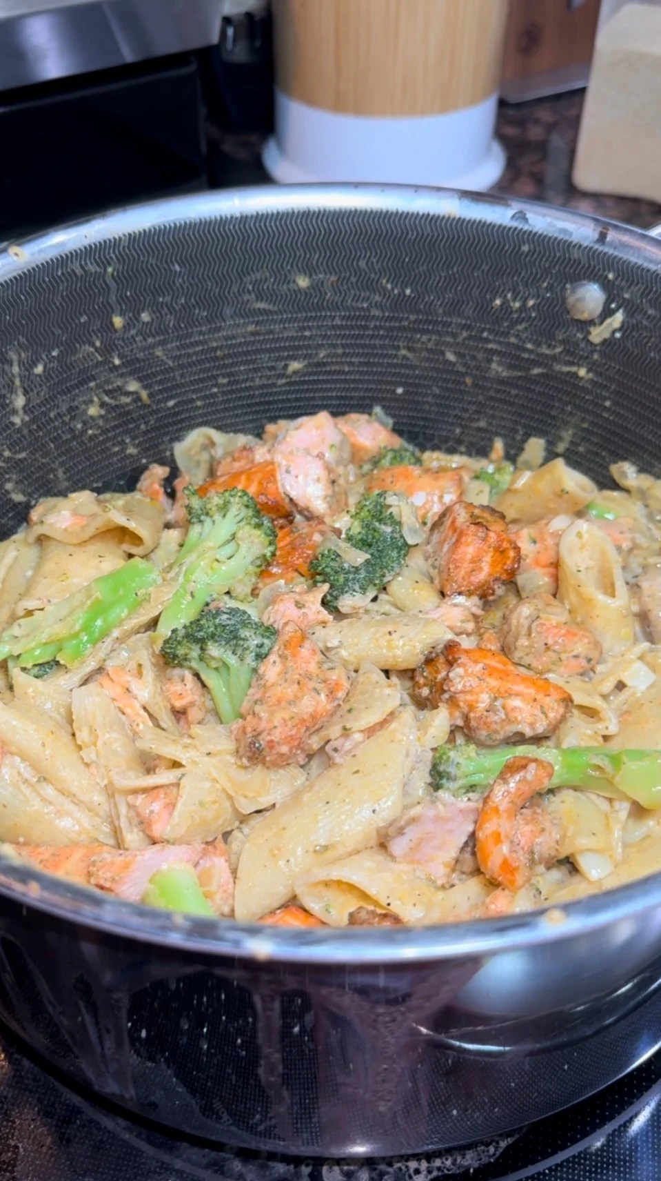 Creamy pasta with broccoli, salmon, and chicken in a black skillet.