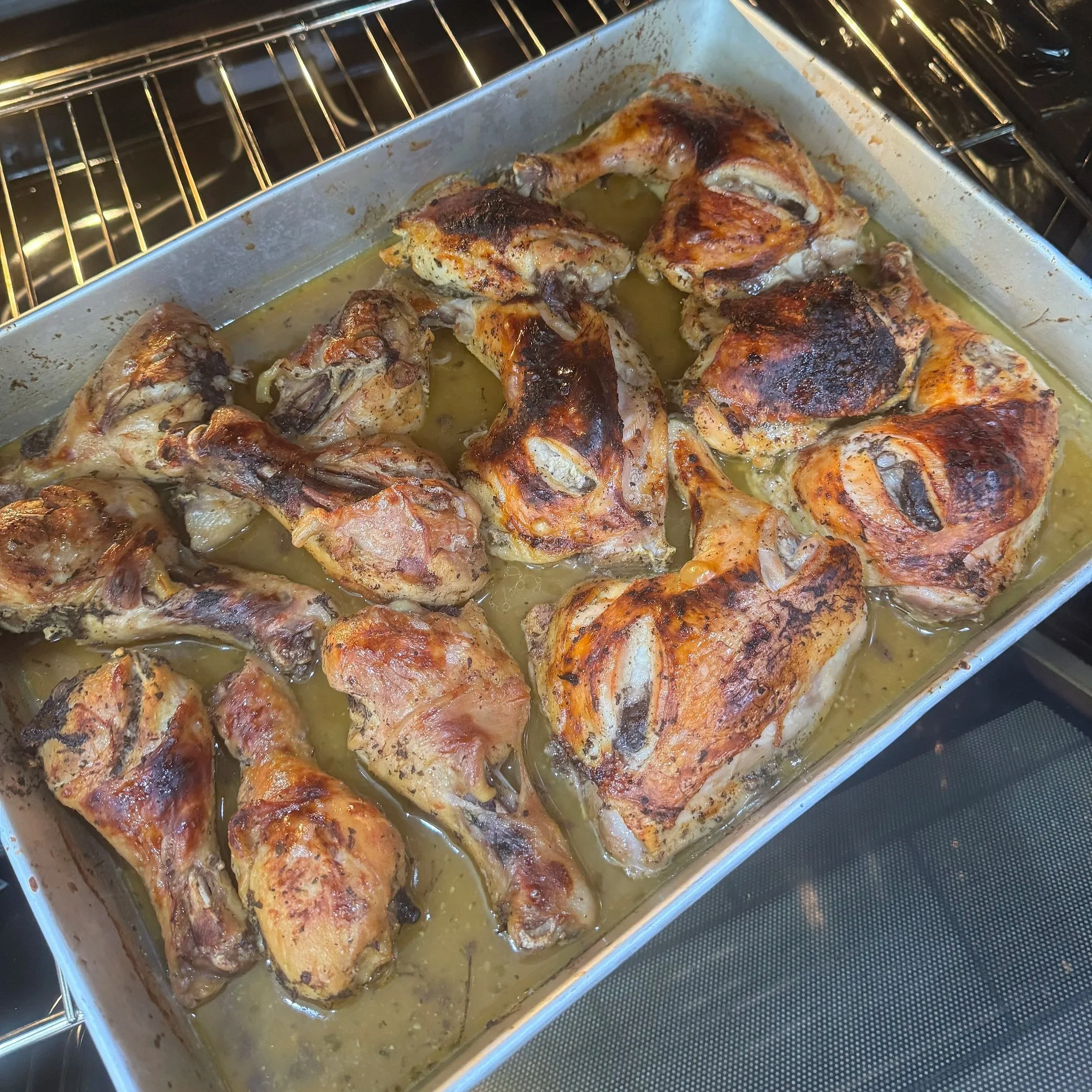 Baked chicken pieces in a baking dish with melted butter and juices, cooked in an oven.