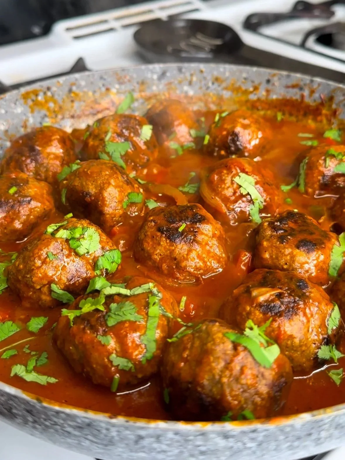 Beef Meatballs in a tomato sauce garnished with chopped cilantro in a frying pan.