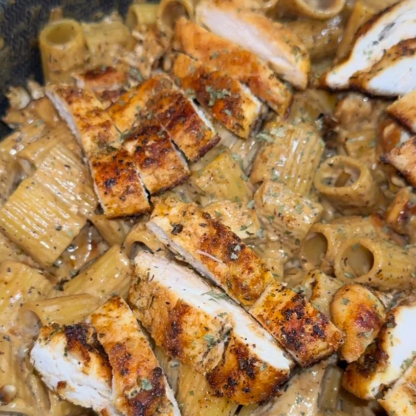 Grilled chicken breast on pasta with creamy sauce and herbs.