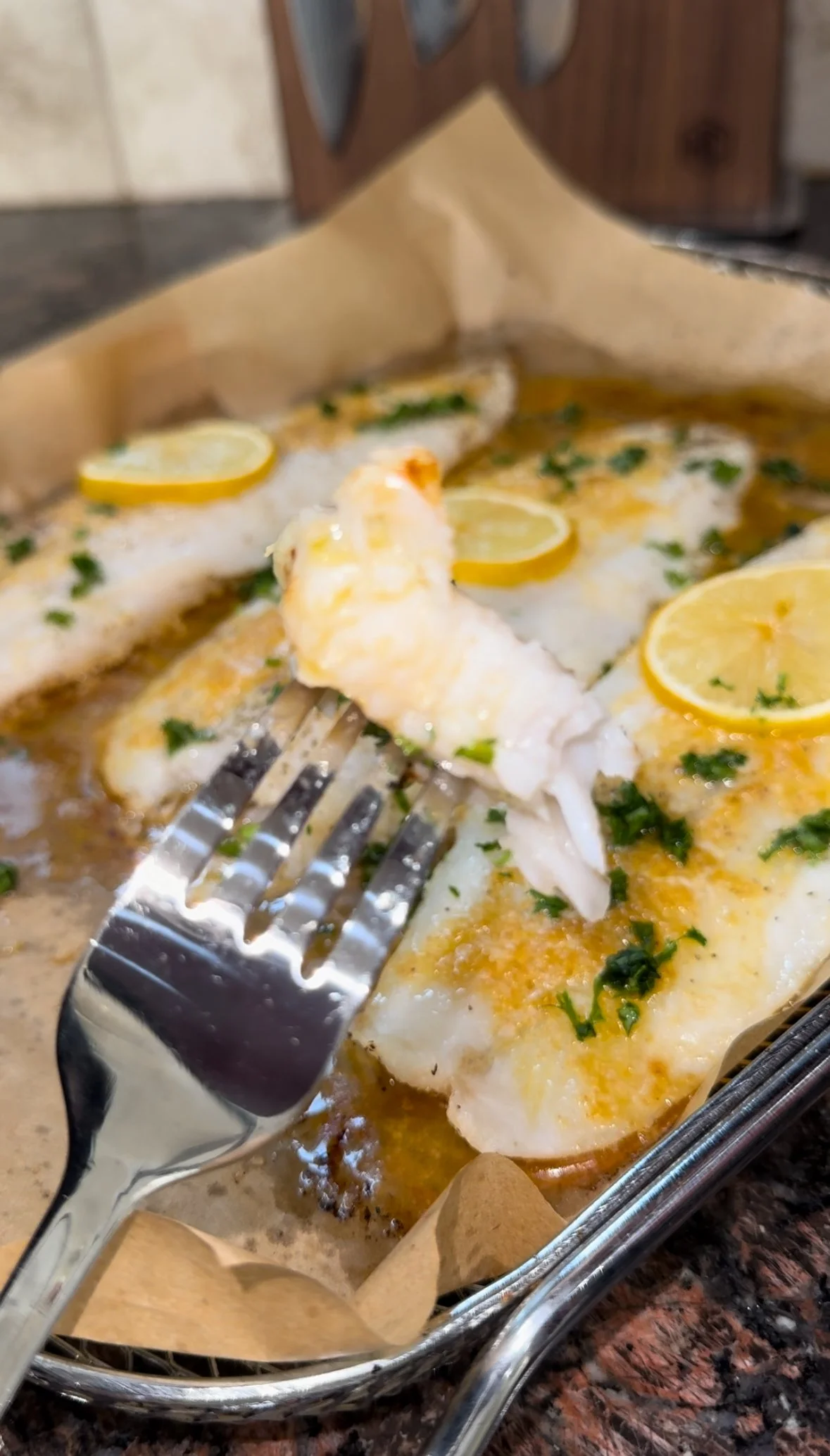 Lemon baked fish fillets garnished with lemon slices and herbs, in a baking dish lined with parchment paper.