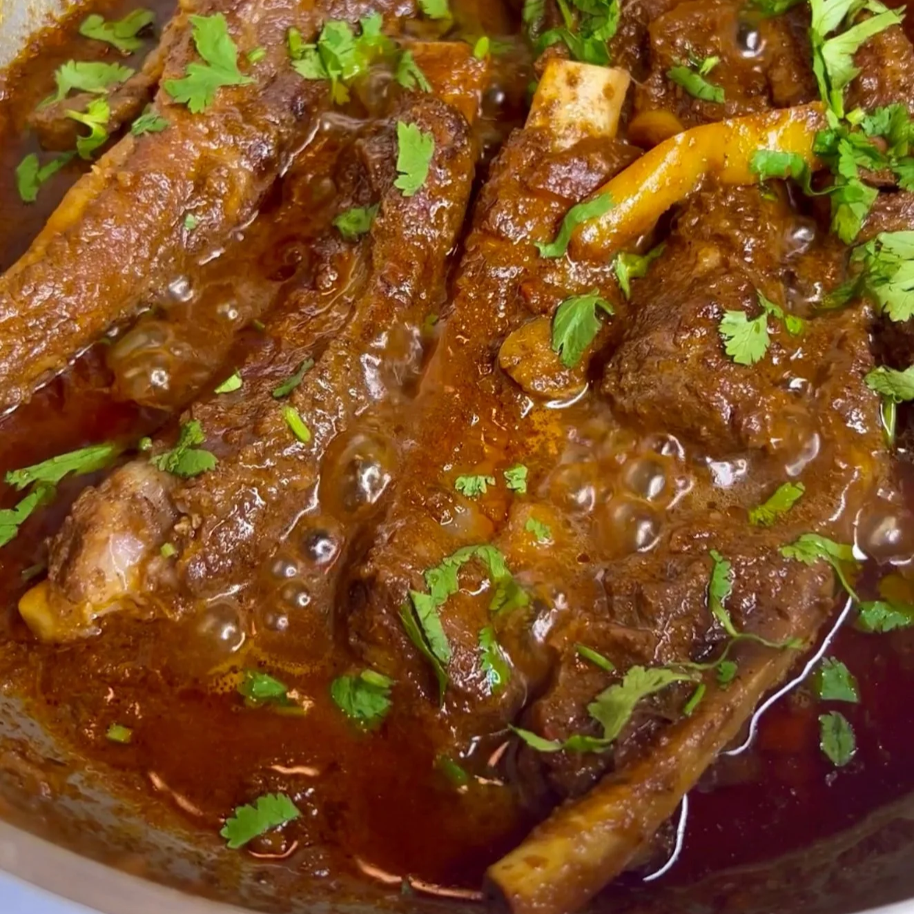 Close-up of cooked stewed beef ribs in a rich, dark brown sauce garnished with chopped cilantro.