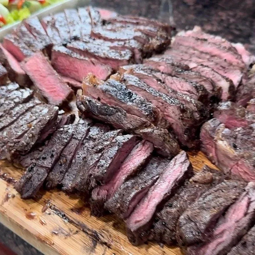 Slices of cooked steak arranged on a wooden cutting board, showing a pink center and seared exterior.