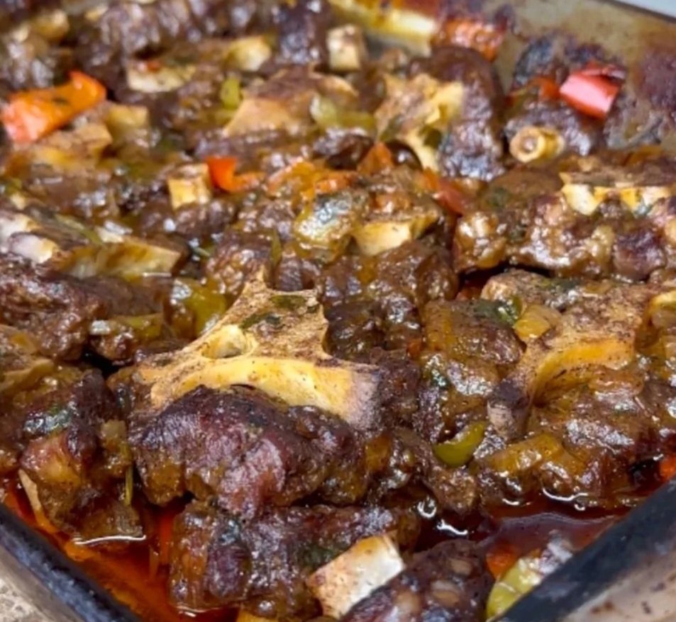 A close-up of cooked beef tail a rich, dark brown sauce with chunks of carrots, vegetables, and gravy.