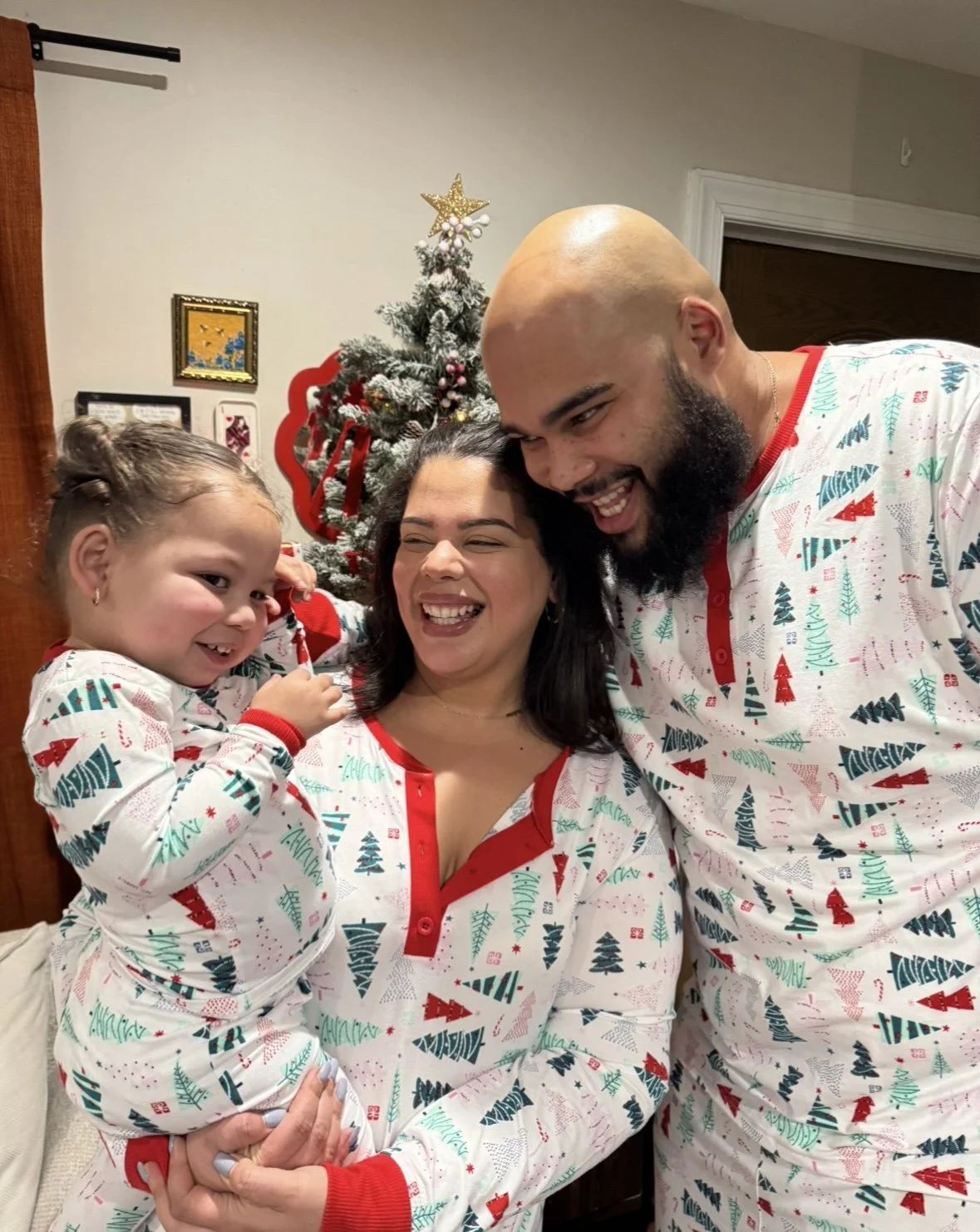 A family dressed in matching Christmas pajamas is gathered in front of a decorated Christmas tree, smiling and enjoying the holiday celebration.