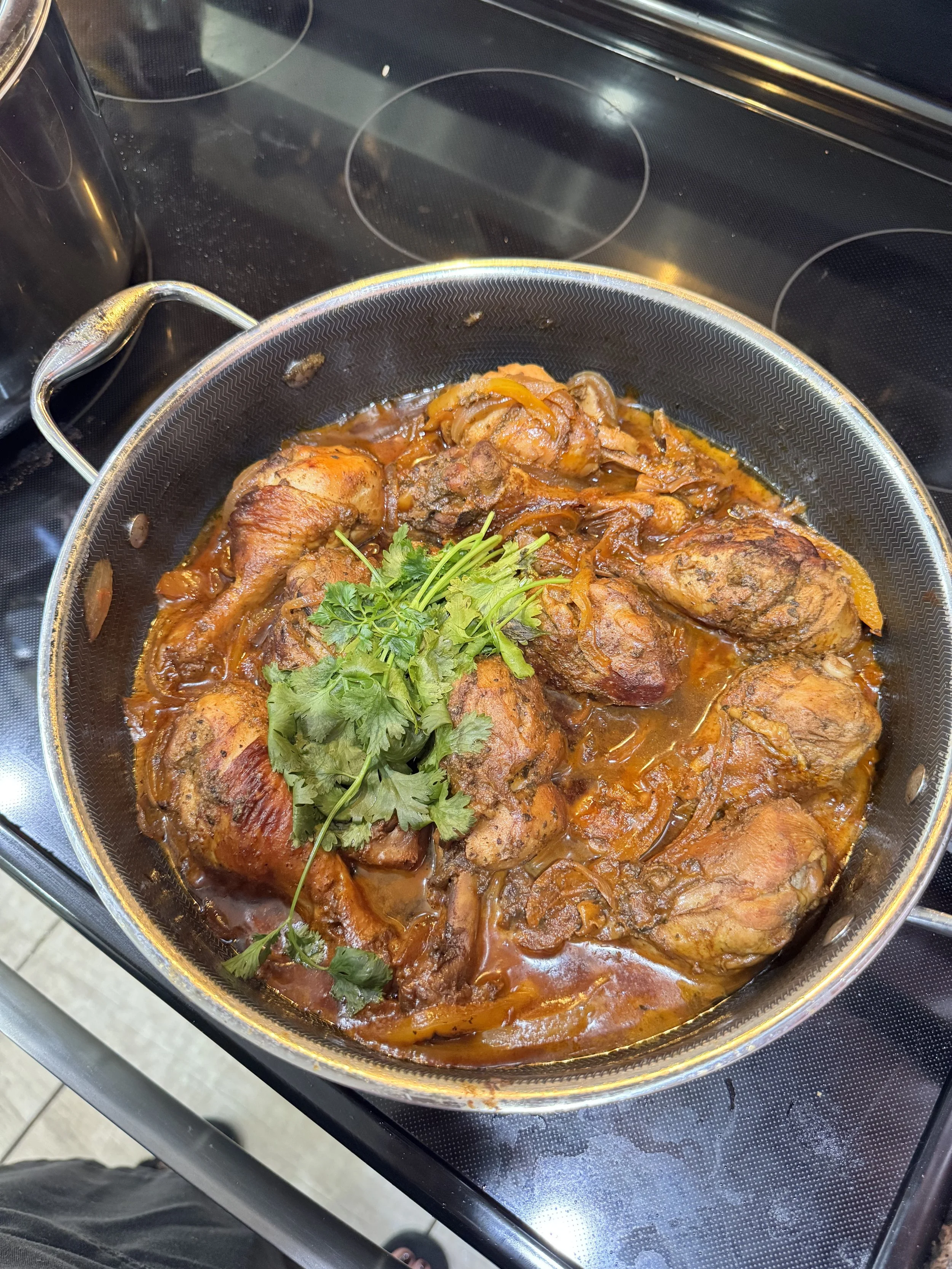 A pot of cooked chicken thighs in a tomato-based sauce garnished with cilantro.