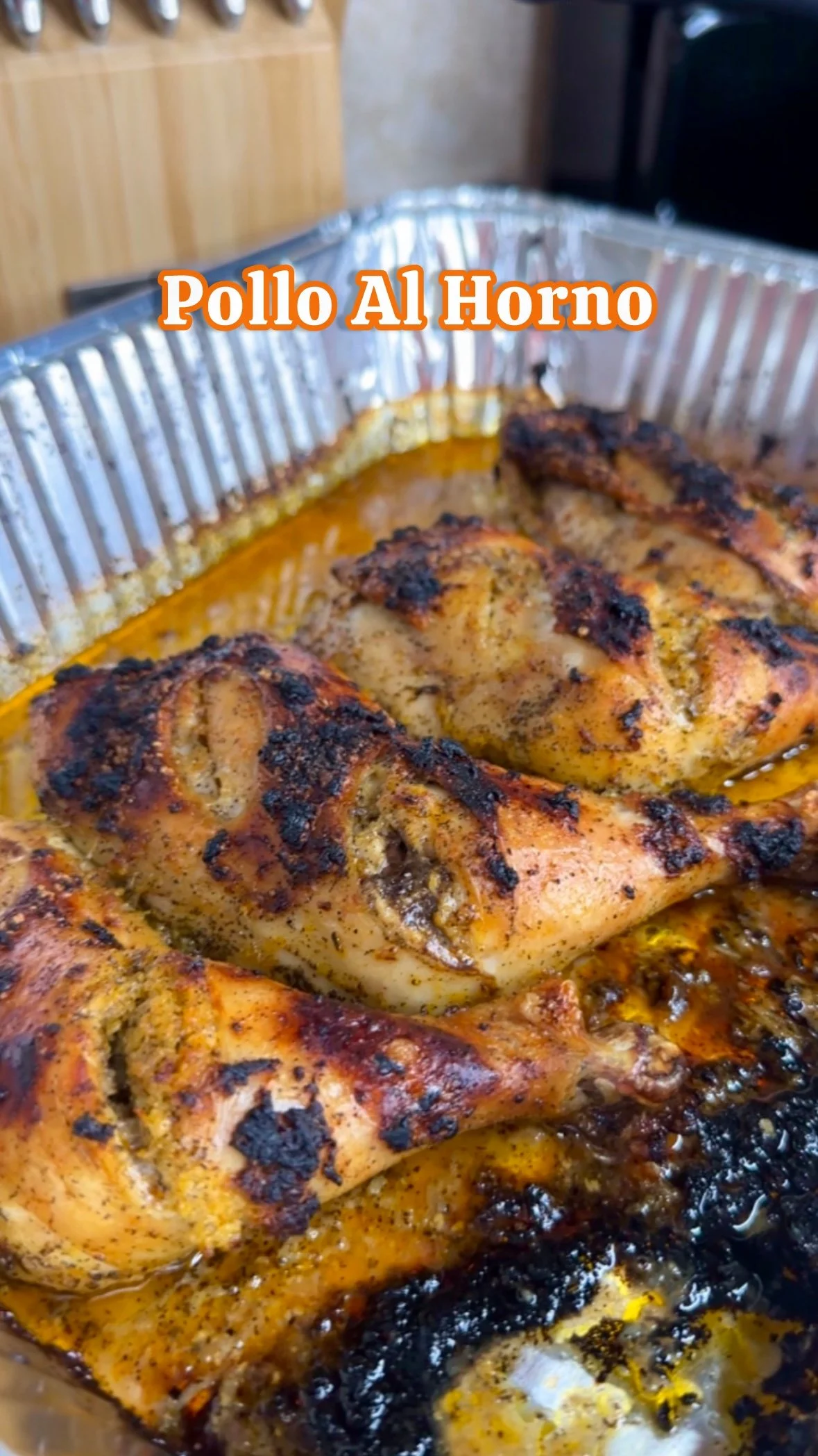 Close-up of roasted chicken with grilled, crispy skin in a metal tray, labeled "Pollo Al Horno."