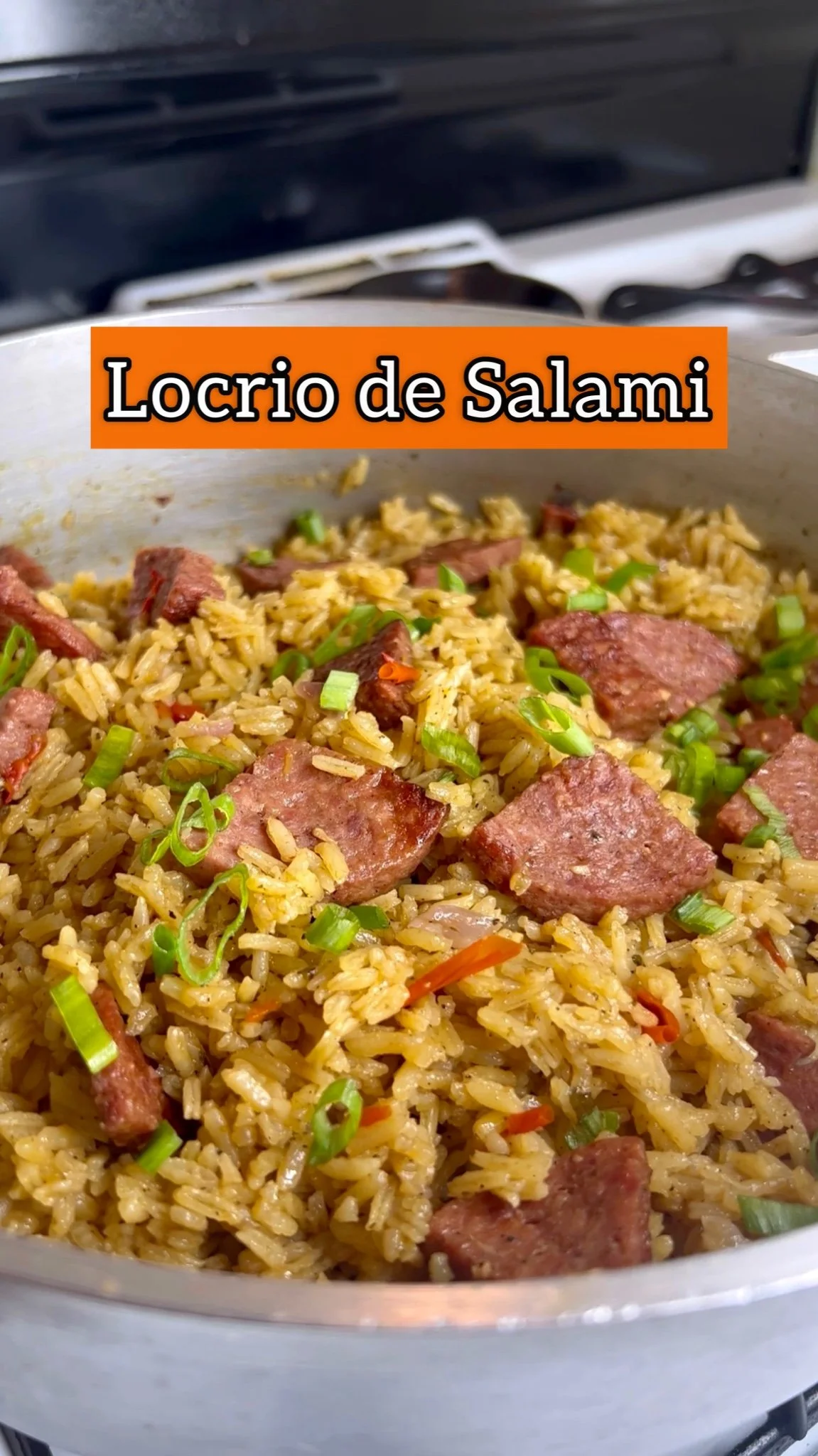 A close-up of cooked rice mixed with sliced sausage and garnished with chopped green onions, labeled as 'Locrio de Salami' in Spanish.