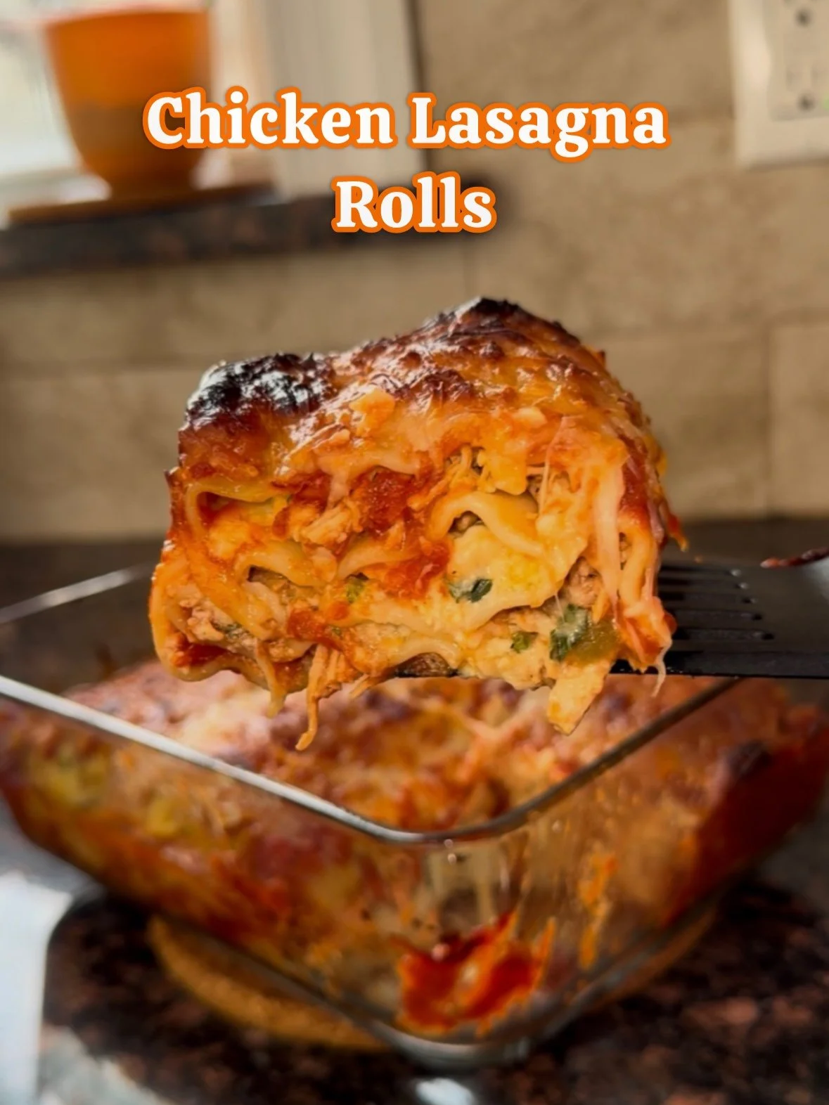 Close-up of a chicken lasagna roll with melted cheese, sauce, and herbs, held above a glass baking dish containing more lasagna rolls.