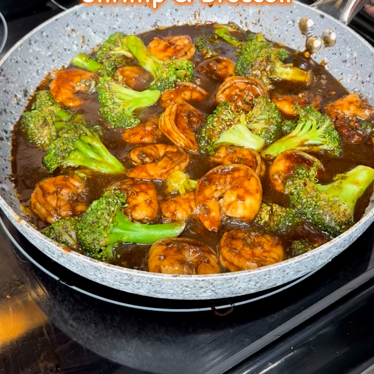 Shrimp and broccoli cooking in a saucy pan on a stove.