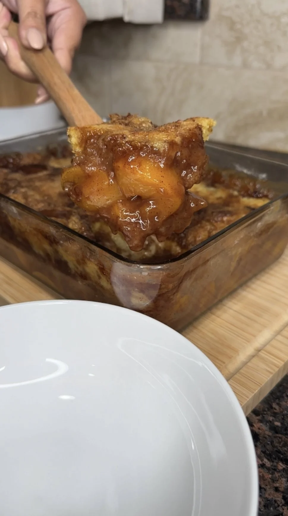 A spoon scooping peach cobbler dump cake from a glass baking dish.