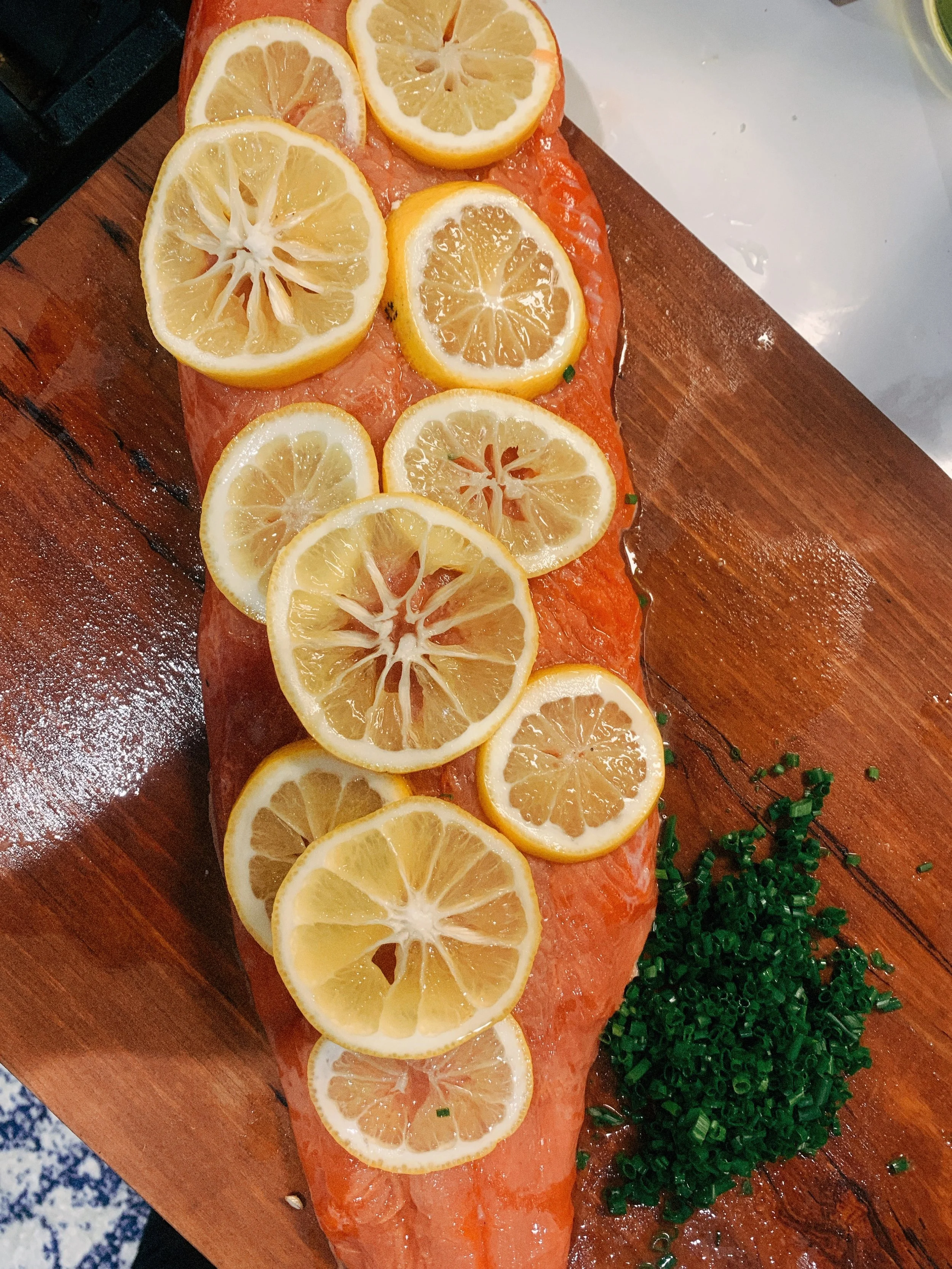 Raw salmon fillet topped with lemon slices, garnished with chopped green onions on a wooden cutting board.