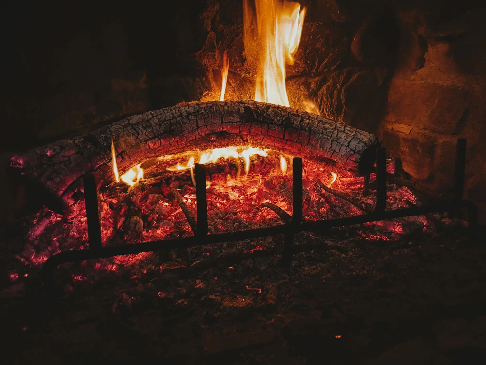 Fire burning with glowing embers and orange flames, surrounded by dark rocks and ashes.