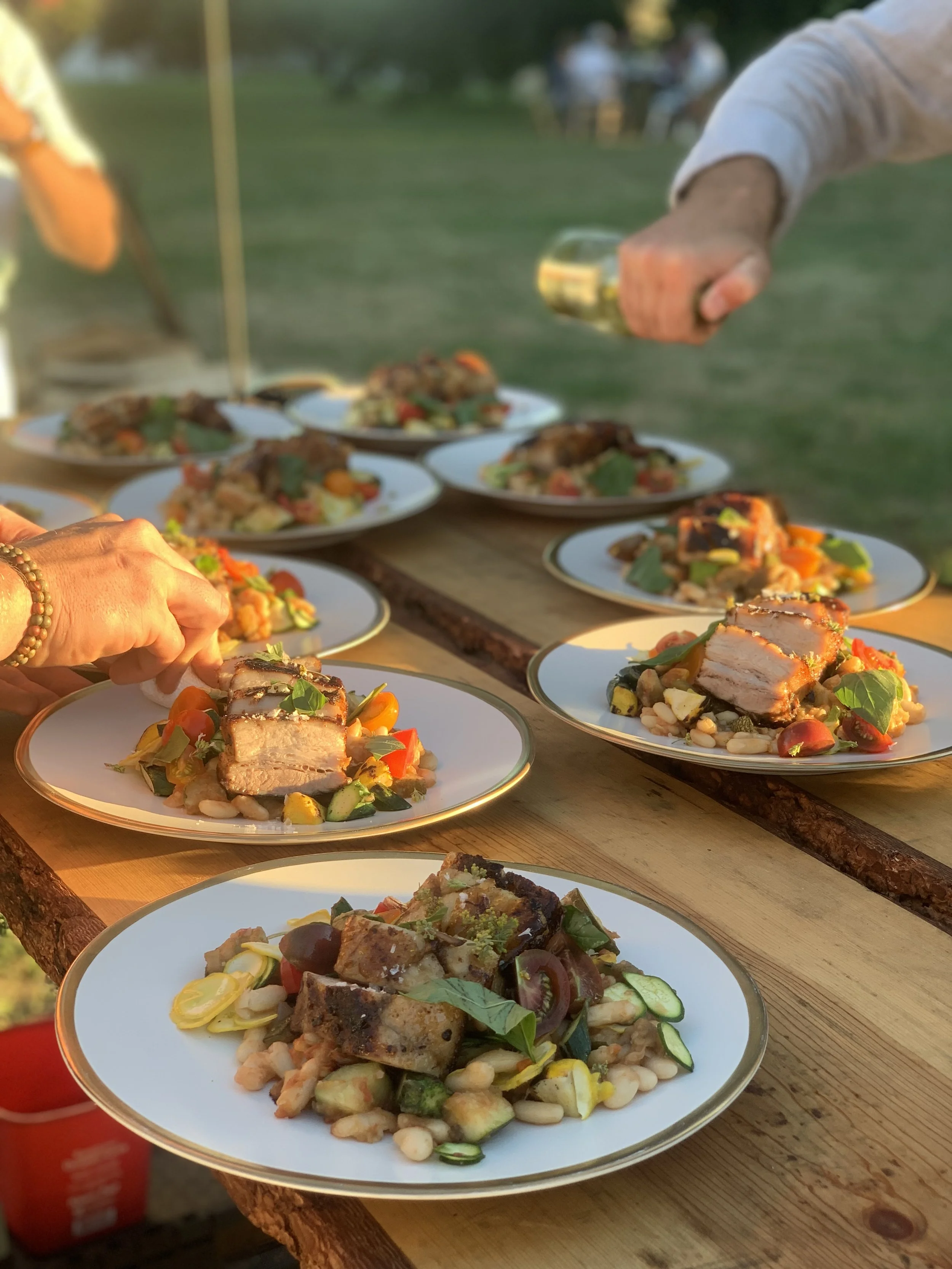 Plates of assorted gourmet food arranged on a wooden table outdoors during a gathering or event.
