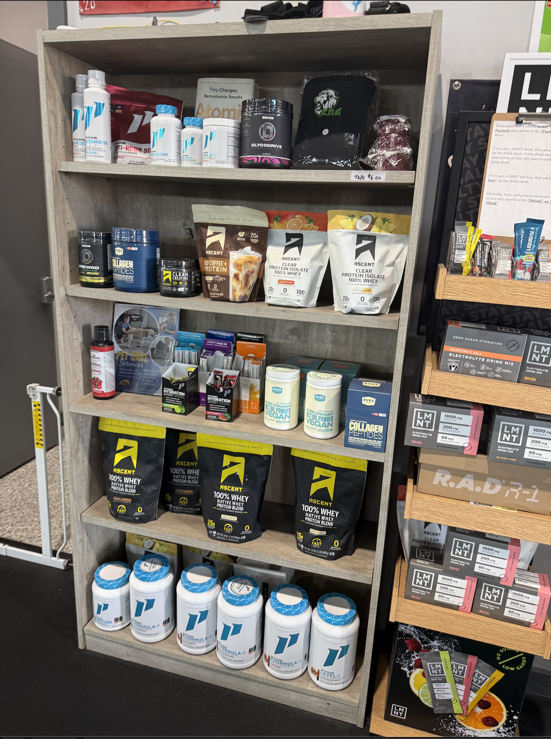 A wooden shelf filled with various fitness and nutrition supplements, powders, and bottles in a store.