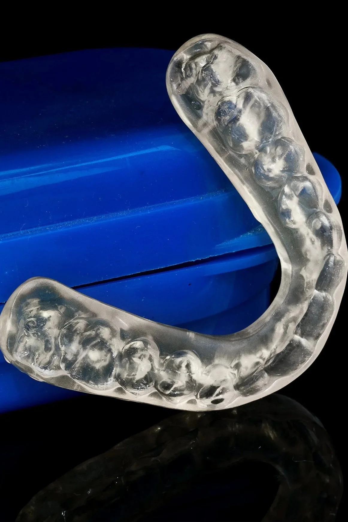 A clear dental night guard resting on a blue container with a black background.