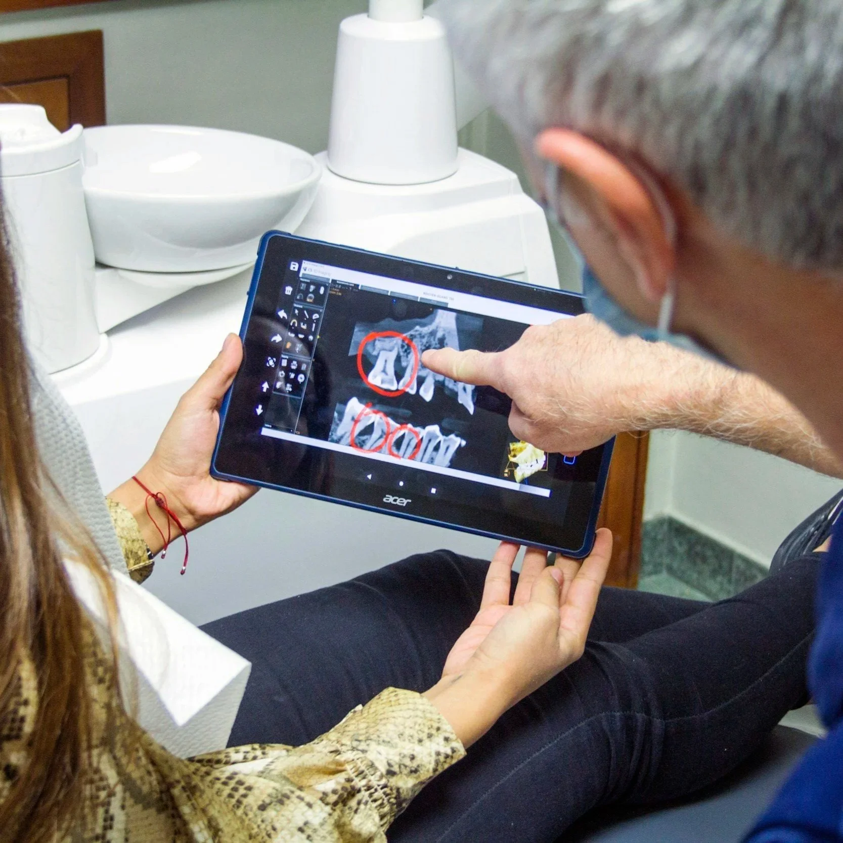 A person holding a tablet with a photo editing program open, showing a photo with red circles drawn around some text. Another person points at the screen, explaining the editing.