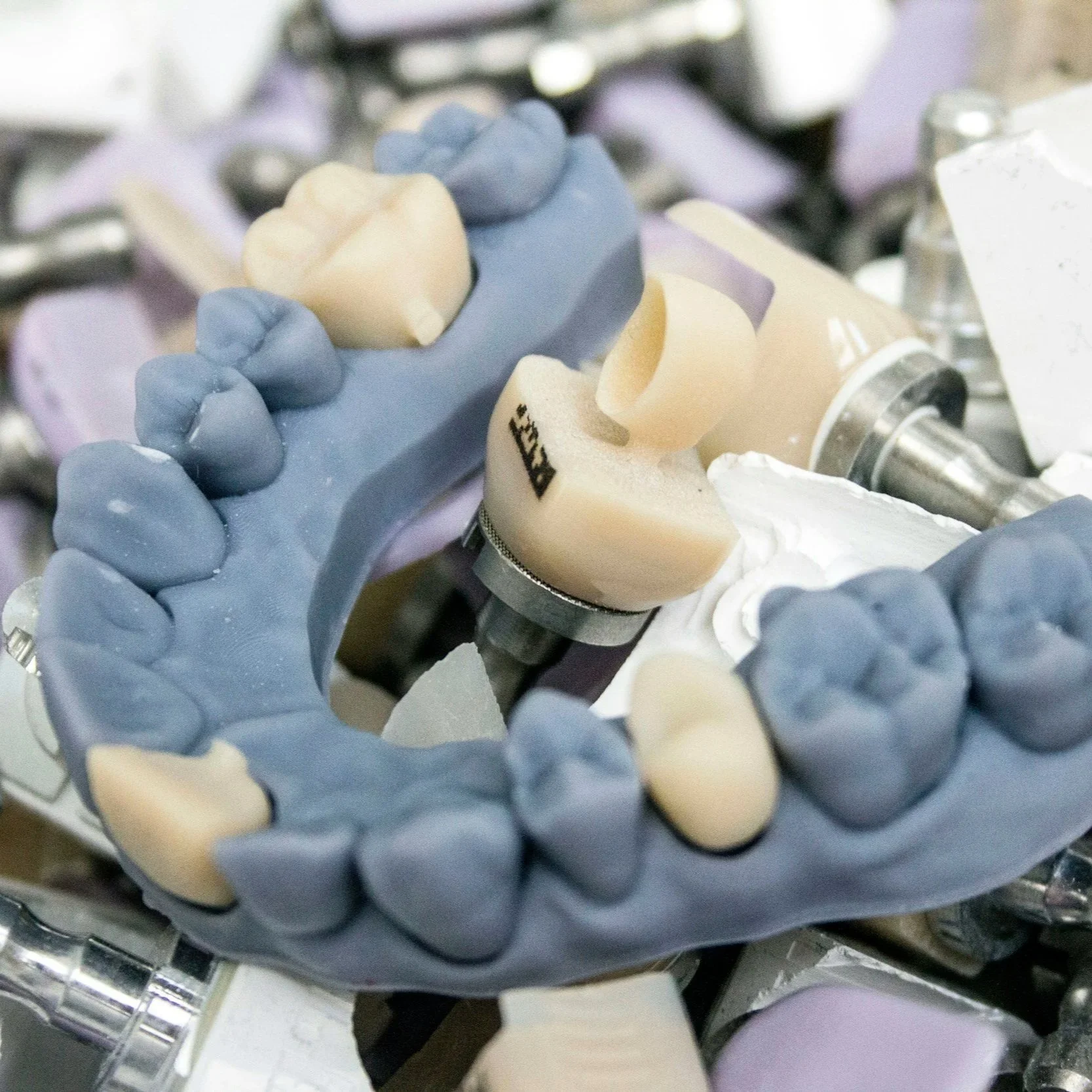 Close-up of dental prosthetics, including a blue silicone impression tray with artificial teeth, dental molds, and dental tools on a tray.