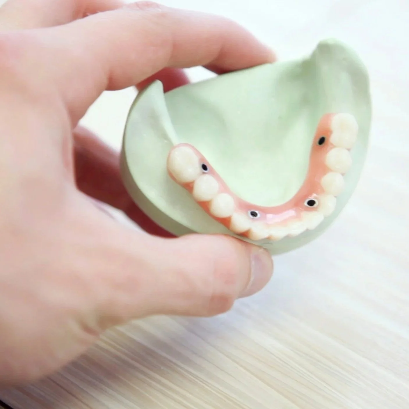 A hand holding a dental model with fake teeth and googly eyes attached.